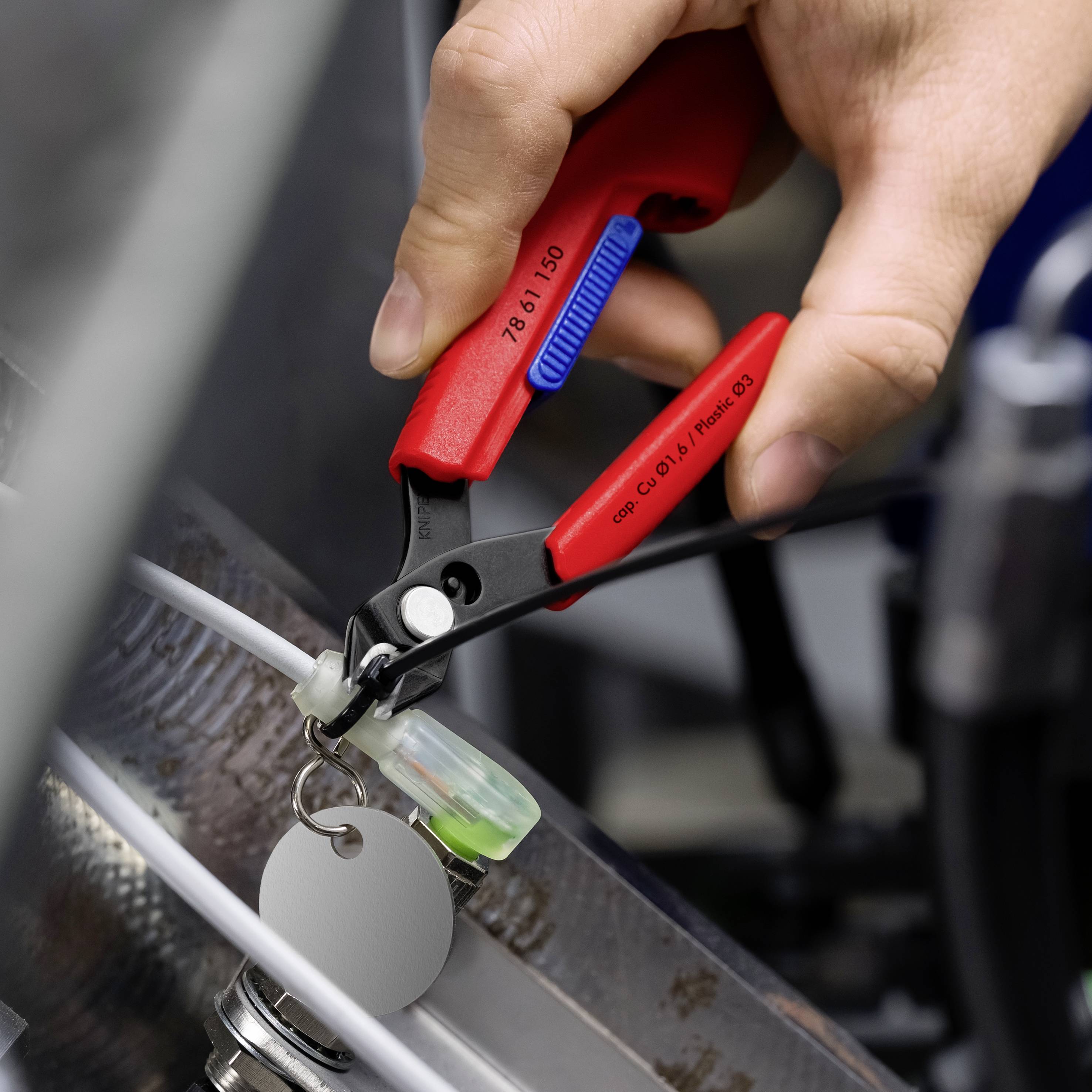 Hand, die einen Drahtabisolierer verwendet, um die Isolierung von einem Kabel zu entfernen, mit einem Schlüsselring und einem Etikett in der Nähe des Arbeitsbereichs.