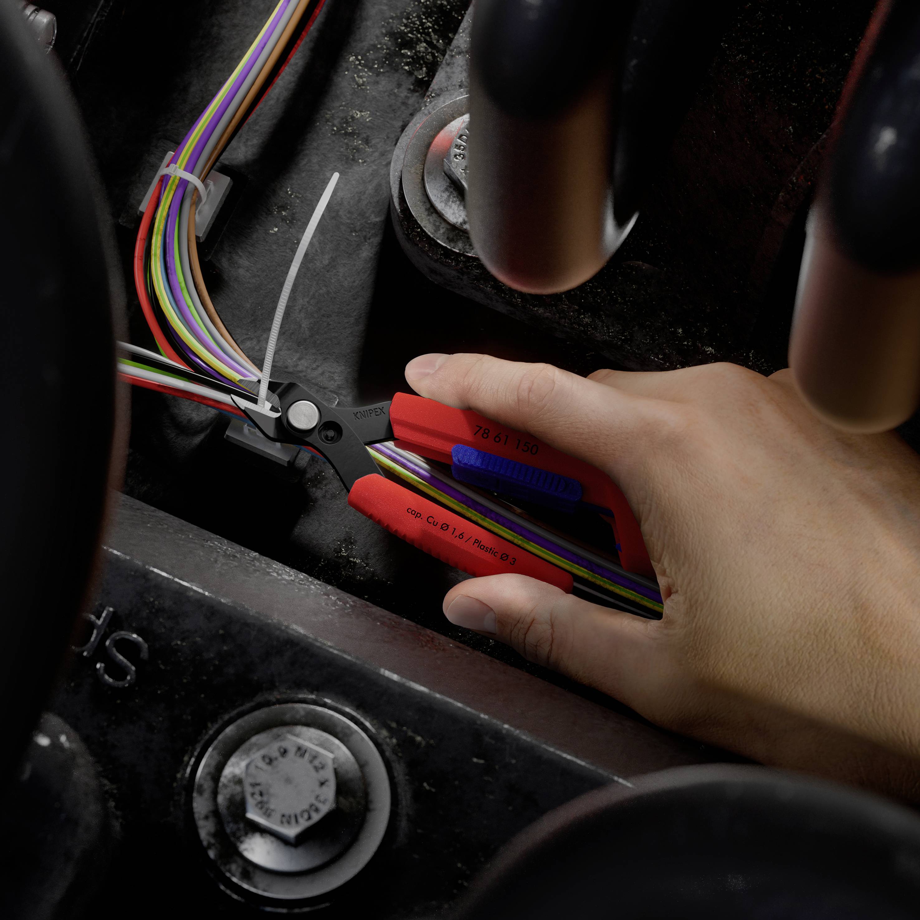 Hand, die Drahtschneider verwendet, um ein Bündel mehrfarbiger elektrischer Drähte in einem Fahrzeug- oder Maschinenraum abzuisolieren.