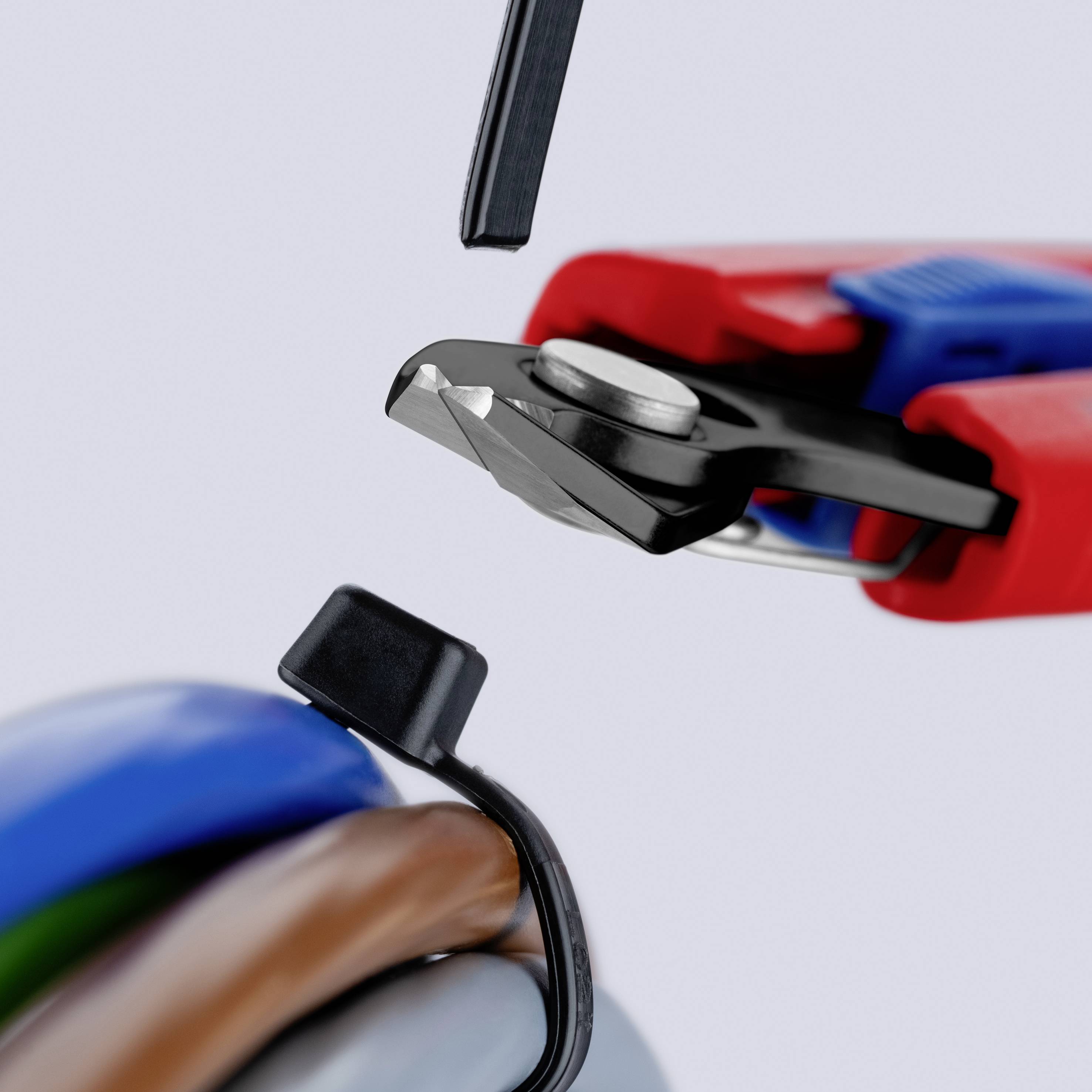 Nahaufnahme eines Abisolators, der die schwarze Isolierung von einem Elektrokabel durchschneidet und die farbigen inneren Drähte freilegt.