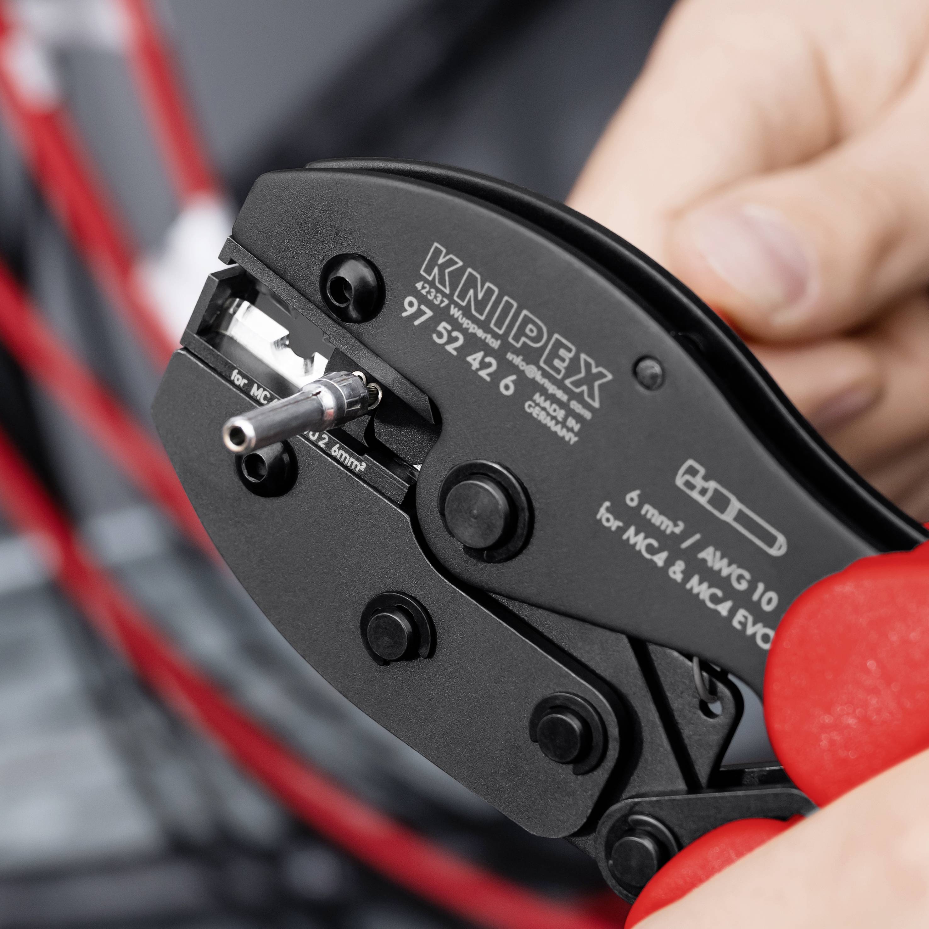 Nahaufnahme einer Hand, die ein KNIPEX-Drahtkrimpmerkzeug verwendet, um einen Metallstecker auf einem Kabel zu crimpen.