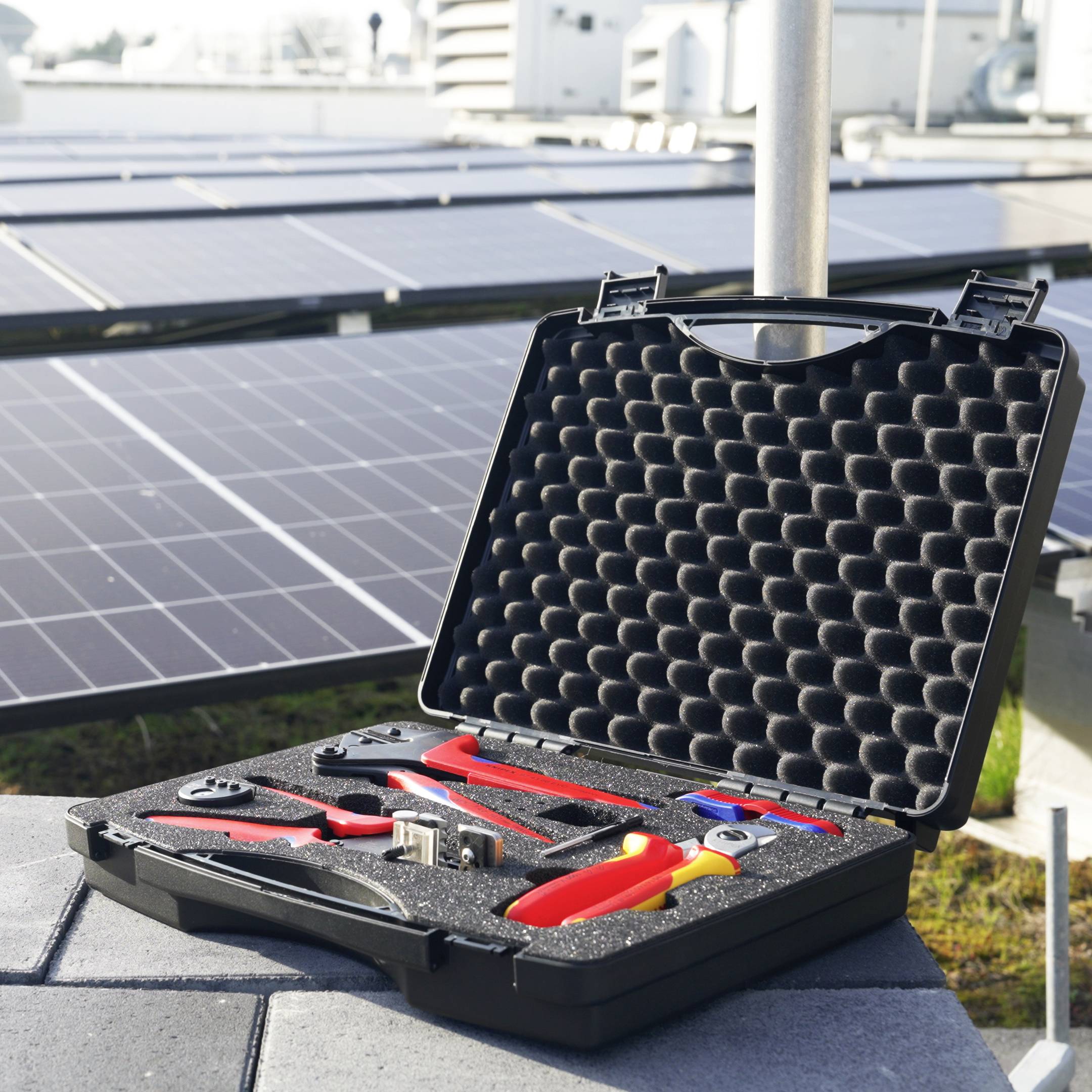 Offener Hartschalenkoffer mit isolierten Handwerkzeugen und Zangen vor Solarpanelen, was auf Wartungsarbeiten an einer Solaranlage hindeutet.