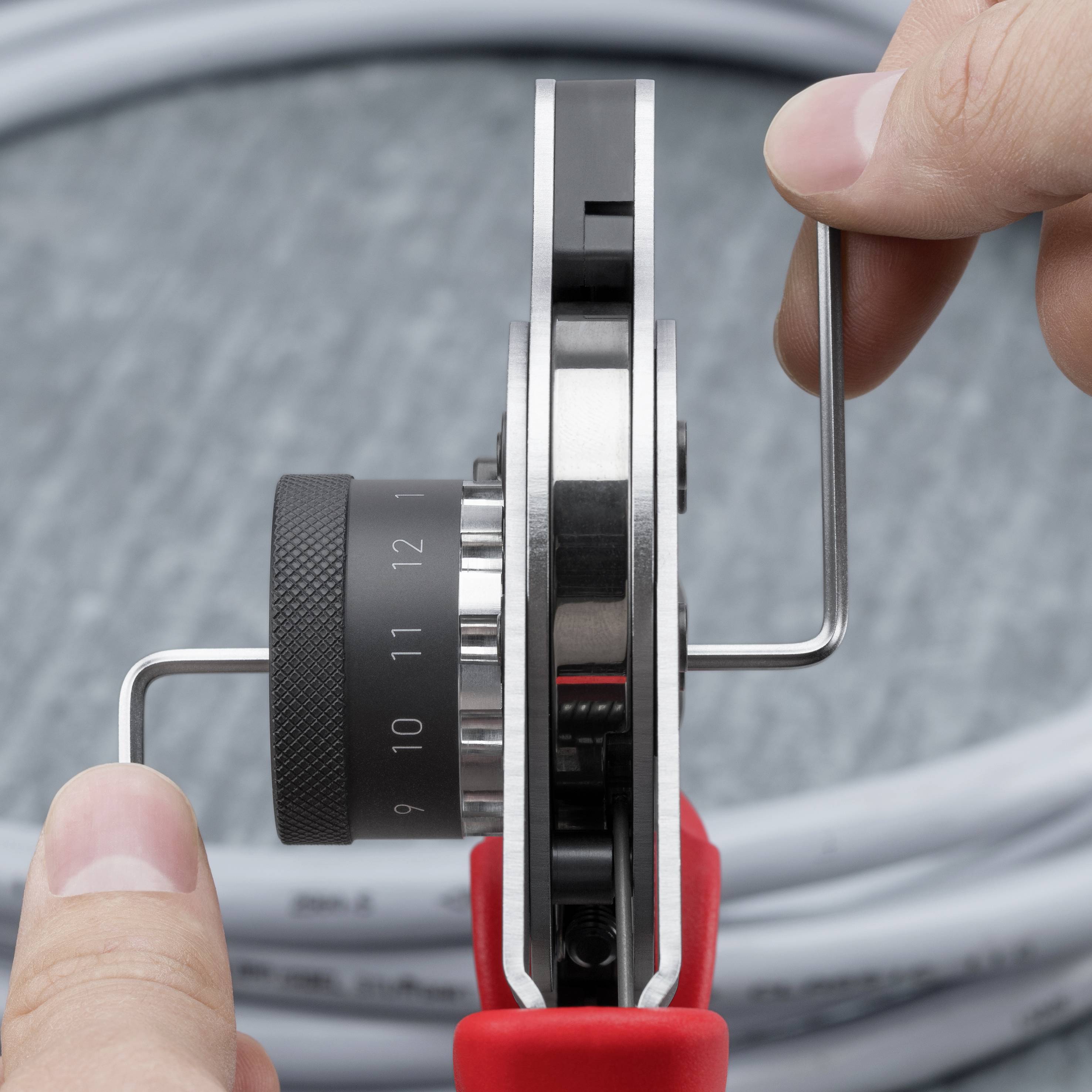 Nahaufnahme von Händen, die ein Präzisions-Messinstrument an einem mechanischen Gerät drehen, während sie den schwarzen nummerierten Steuerring einstellen.