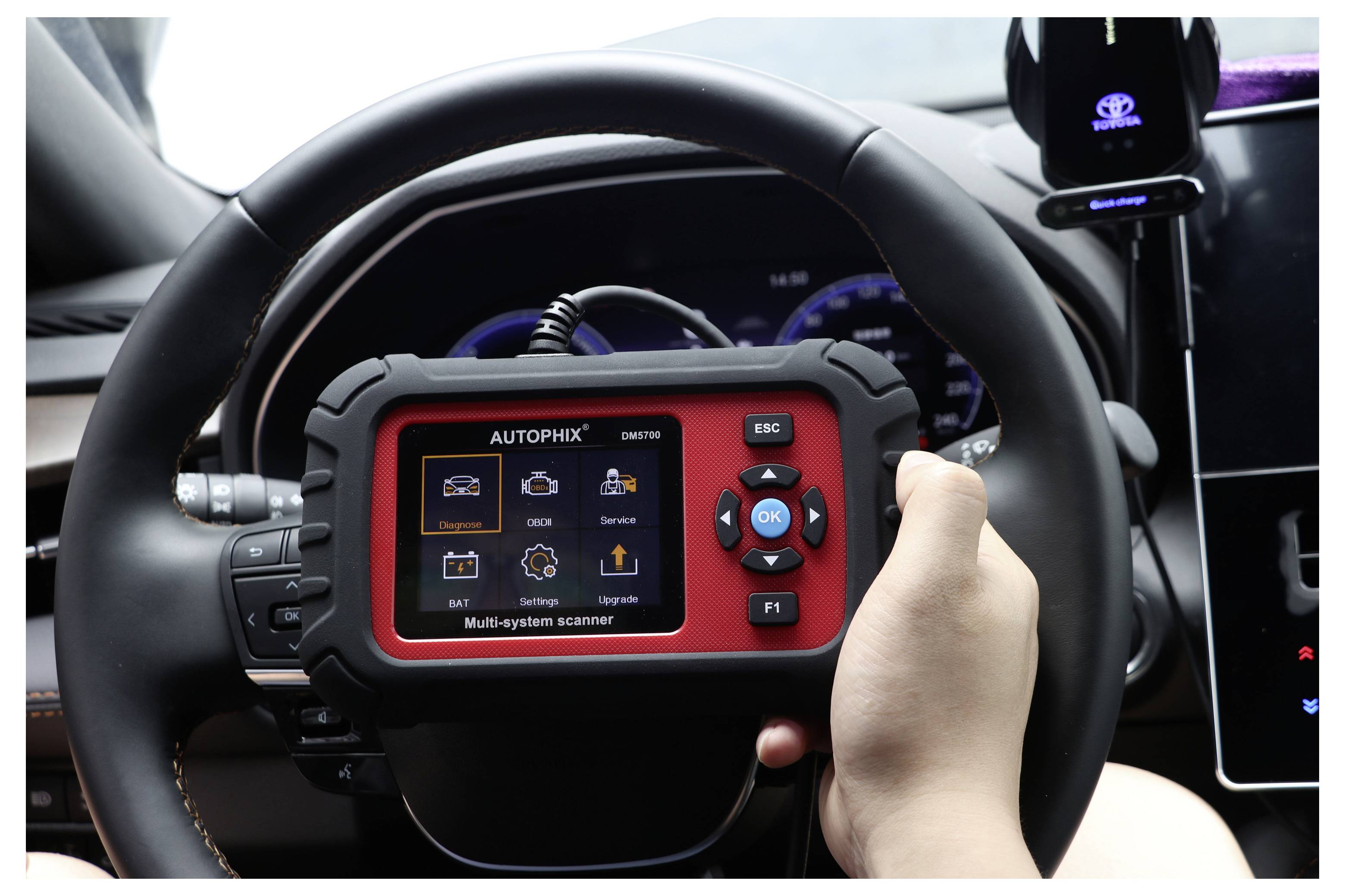 Tragbarer AUTOPHIX Kfz-Diagnosescanner mit einem Mehrschicht-Menü, gehalten vor einem Fahrzeuglenkrad im Inneren eines Autos.