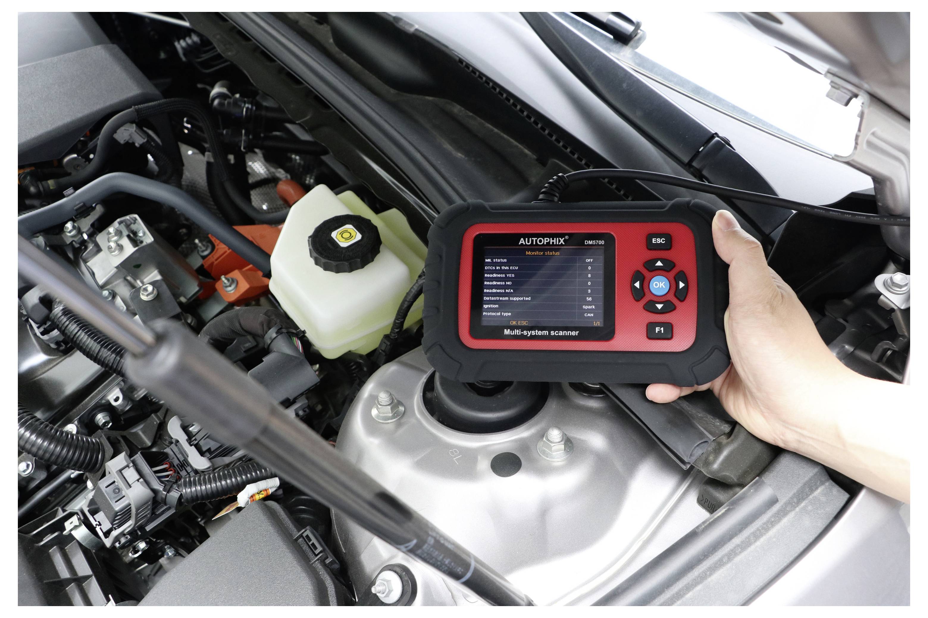 Hand hält einen Autophix-Automobilscanner über einen Motorraum, überprüft die Diagnose in der Nähe der Batterie und des Bremsflüssigkeitsbehälters.