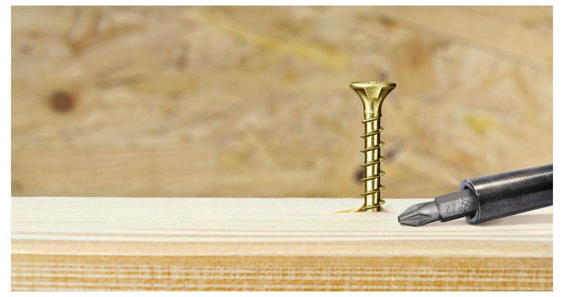 Nahaufnahme eines Schraubendrehers, der eine goldene Schraube in ein Holzbrett treibt, vor einem unscharfen Holzhintergrund.