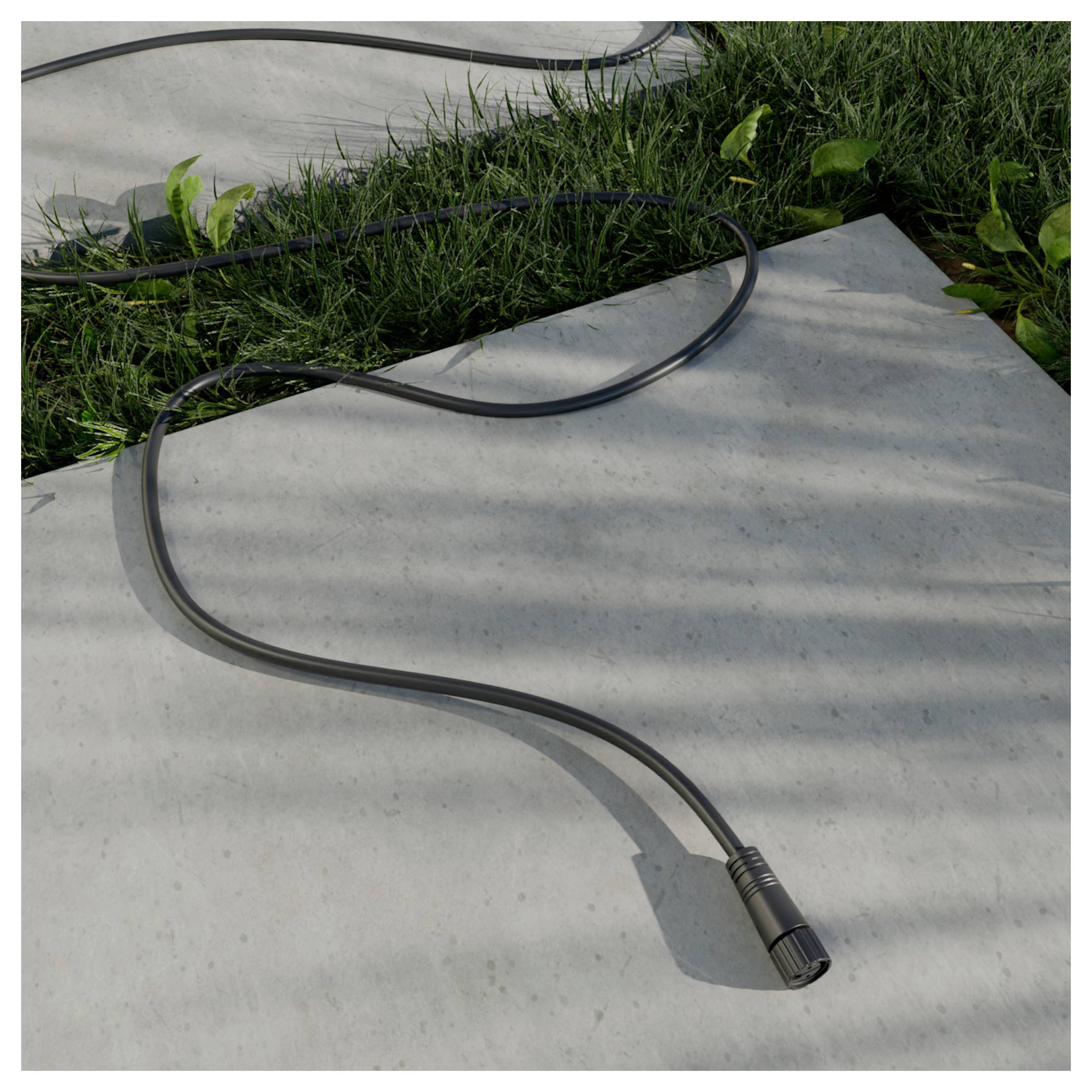 Schwarzes Kabel oder Schlauch in S-Form über einen Betonweg neben Gras liegend, mit einem sichtbaren Steckerende.