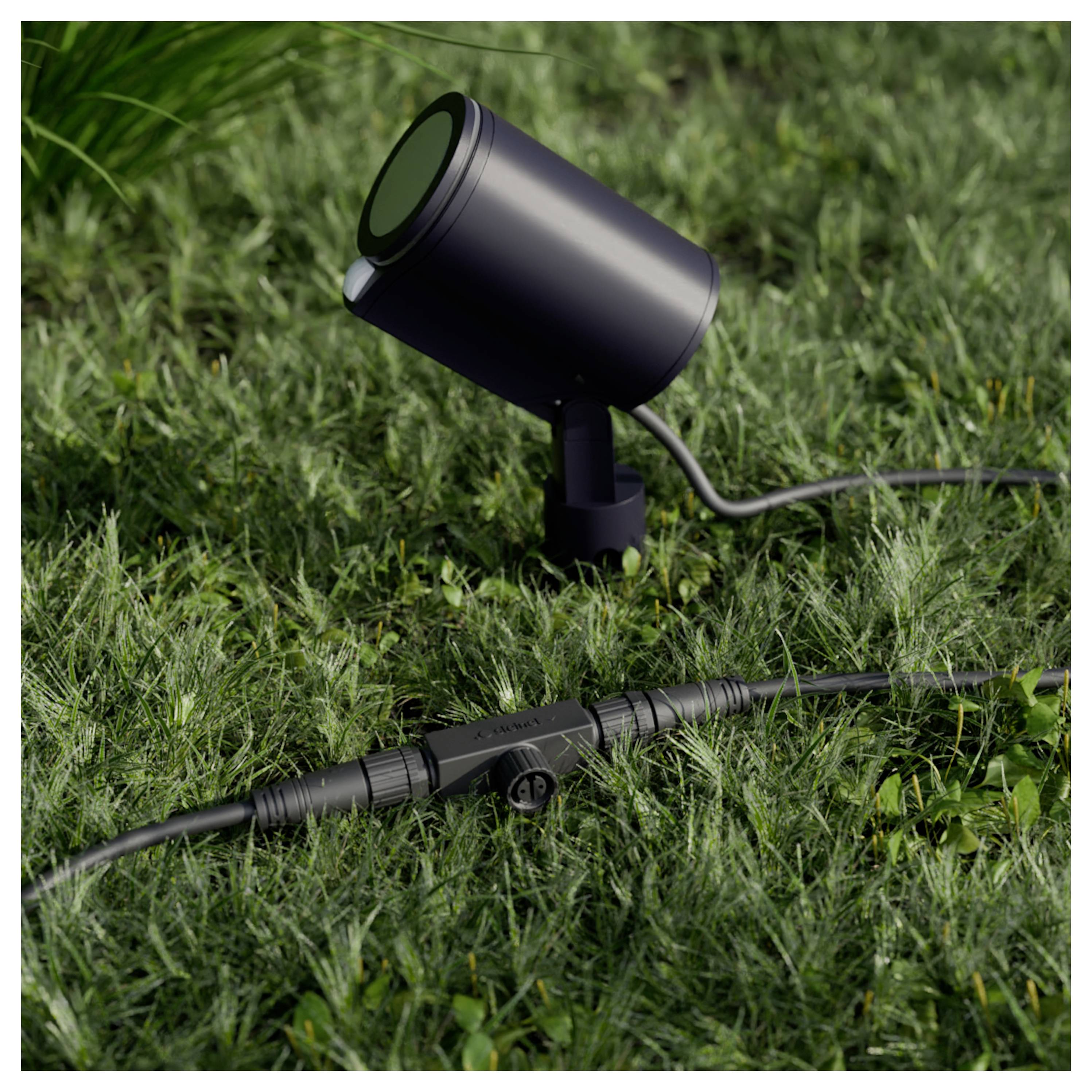 Schwarzer Outdoor-Landschaftsstrahler auf Gras mit angeschlossenem Niederspannungskabel und Inline-Stecker.