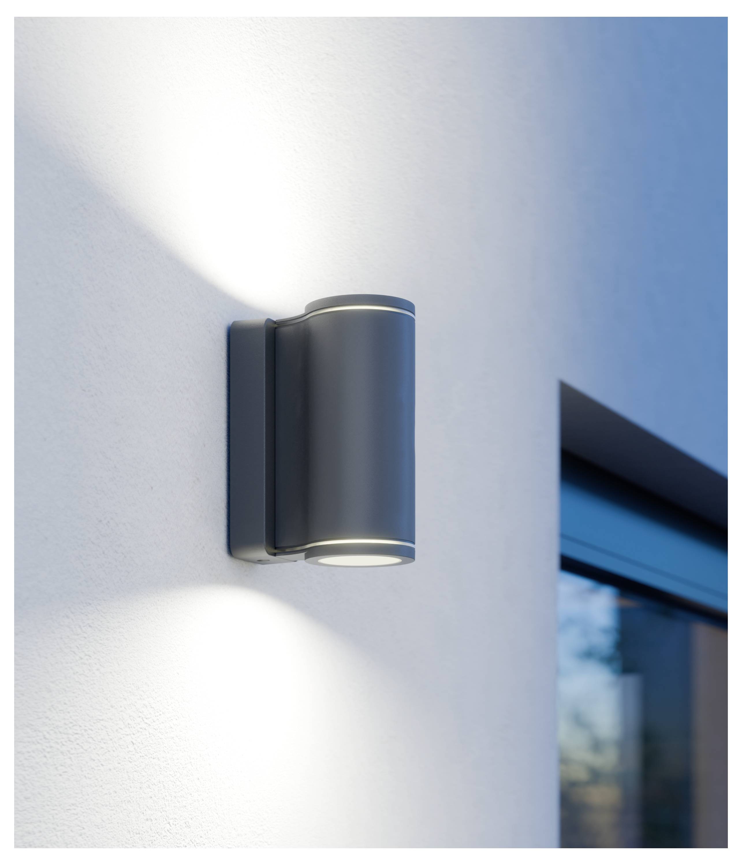 Außenwandleuchte an einem weißen Gebäude, die warmes Licht oben und unten neben einem Fenster wirft.