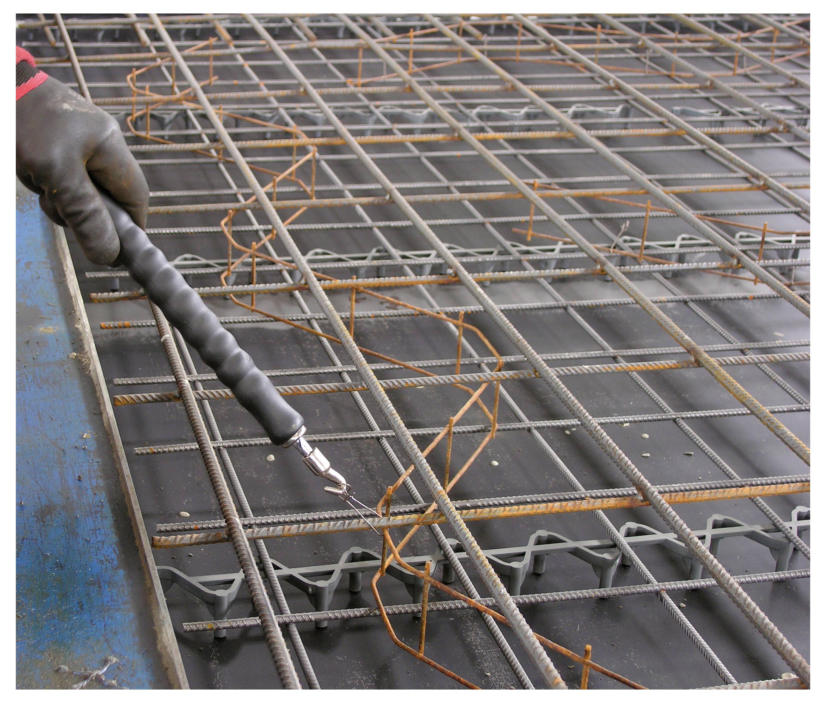 Handschuhgetragener Arbeiter sprüht Korrosionsschutzlack auf ein Stahlbewehrungsgitter auf einer Baustelle.