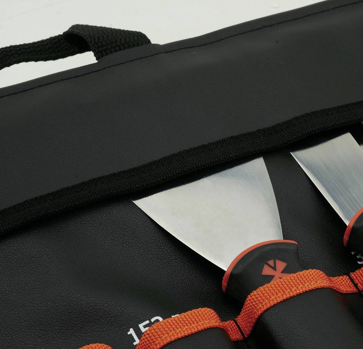 Nahaufnahme eines schwarzen Transportkoffers mit orangefarbenen Riemen und zwei silbernen Messerklingen, die in den vorderen Taschen teilweise sichtbar sind.