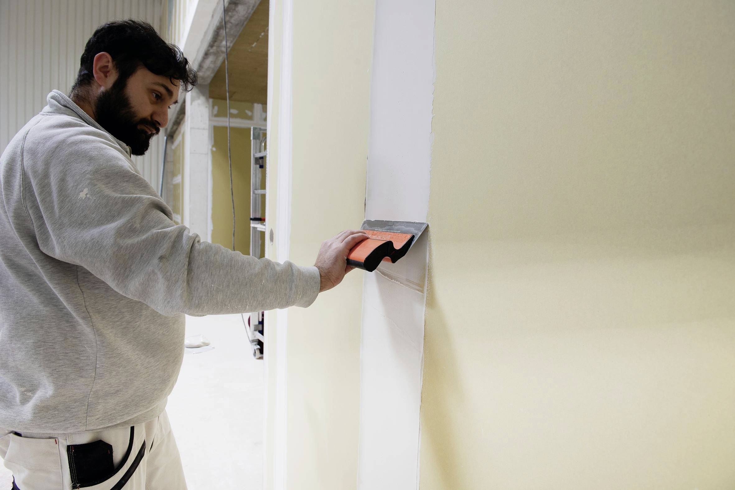 Ein Mann glättet frischen Putz mit einer Kelle an einer Wand während einer Innenrenovierung.