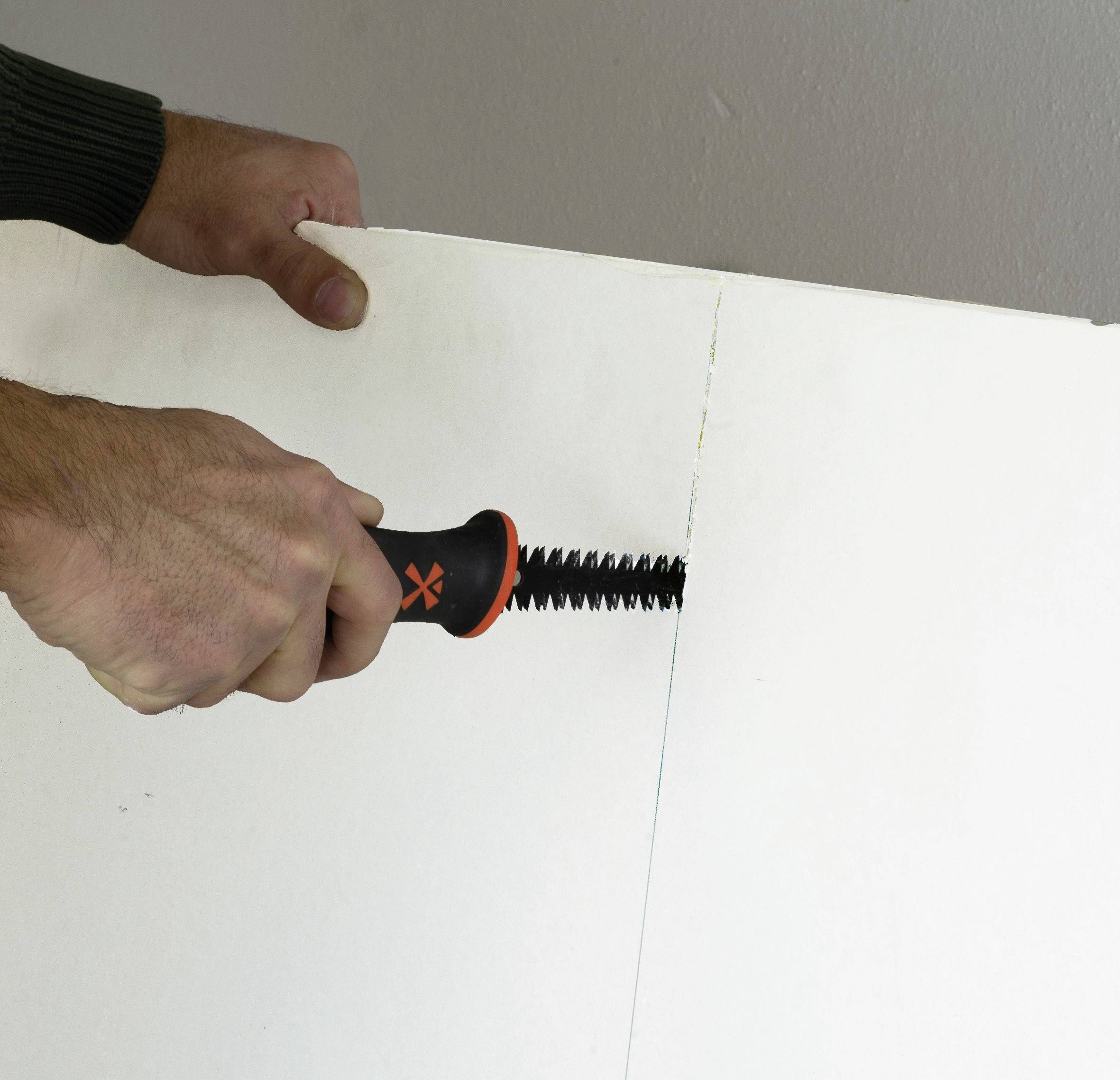 Hände benutzen ein schwarz-oranges Werkzeug, um zwei weiße Schaumstoffplatten an einer Naht auseinanderzuhebeln.