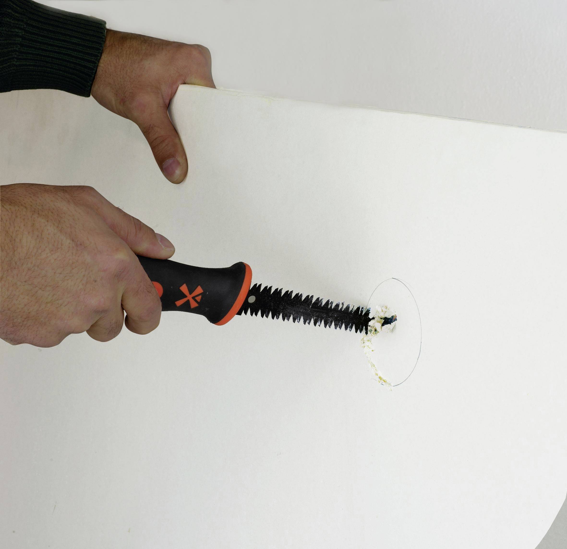 Hände verwenden ein gezahntes Handwerkzeug, um ein kreisförmiges Loch in einer weißen Tafel oder Wandplatte zu schneiden.