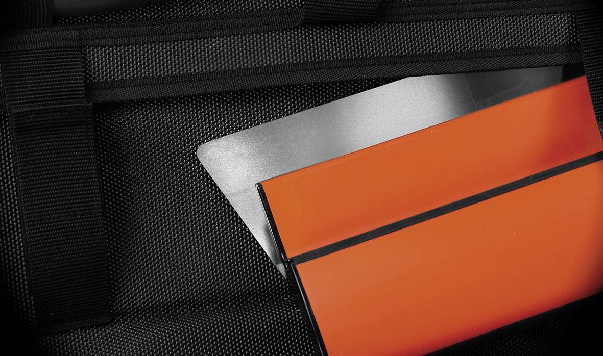 Orangener rechteckiger Ordner oder Aktenordner mit schwarzem Streifen, teilweise in eine schwarze Netztasche oder ein schwarzes Netzfutteral gesteckt.