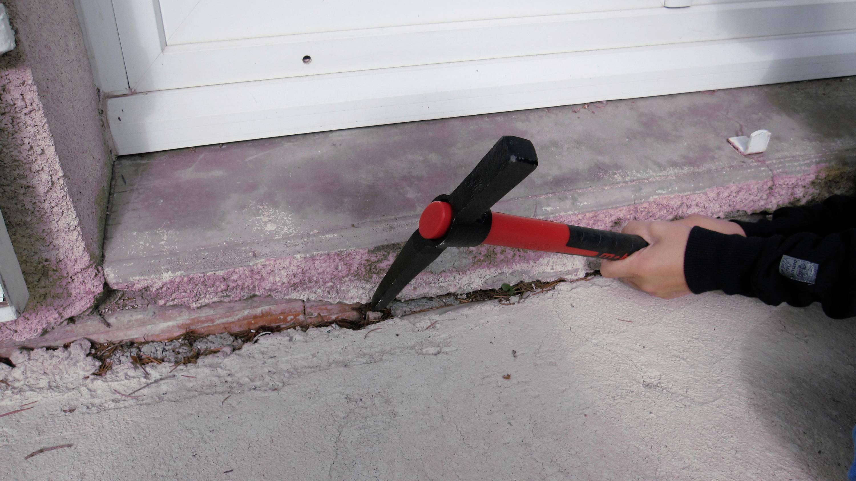 Person, die mit einem Brecheisen Risse im Beton an der Basis einer Außenwand oder Fensterbank abbricht.