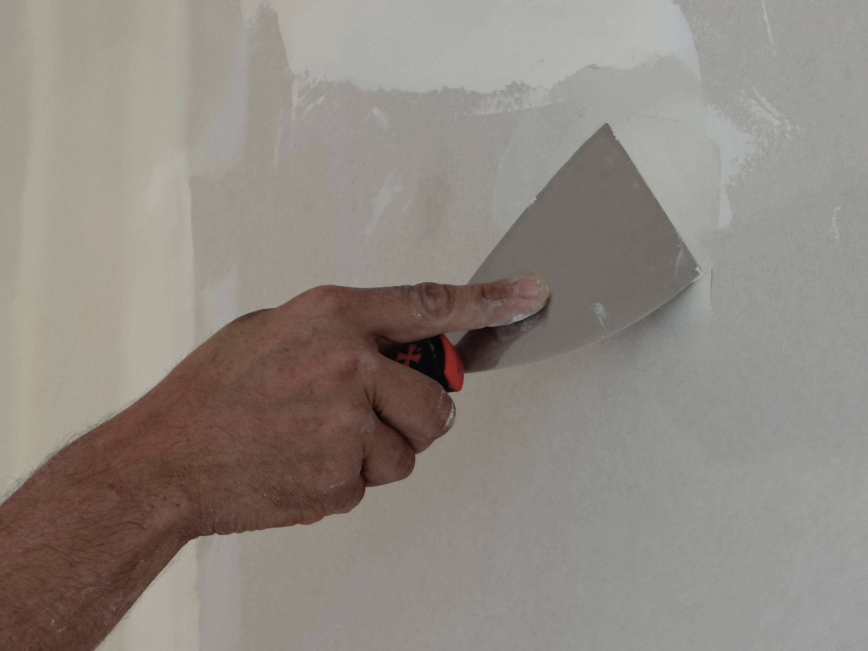 Hand mit einem Spachtel zum Auftragen von Gipskartonmasse auf eine Wand während der Hausreparatur.