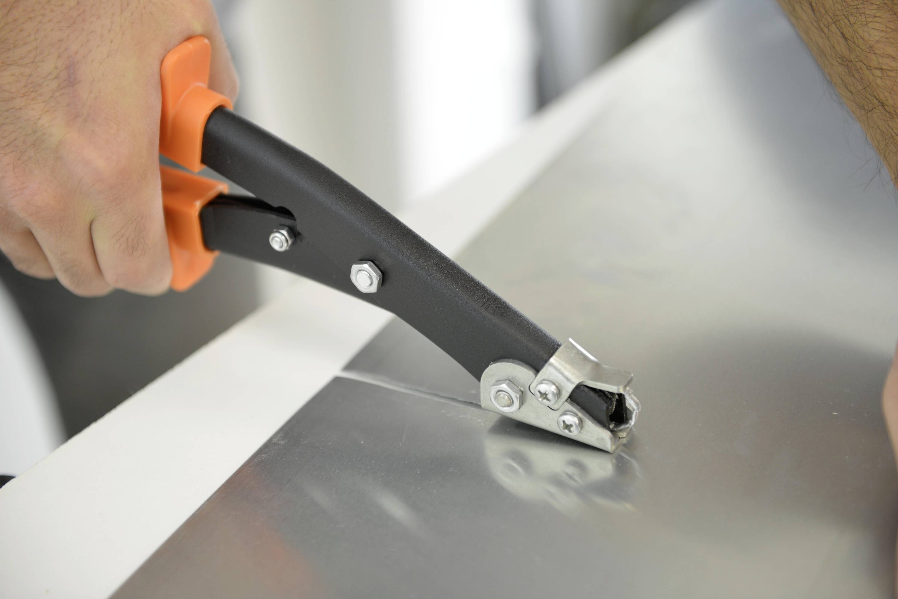 Nahaufnahme einer Person, die orangefarbene Metallscheren verwendet, um ein Blatt glänzendes Metall zu schneiden.