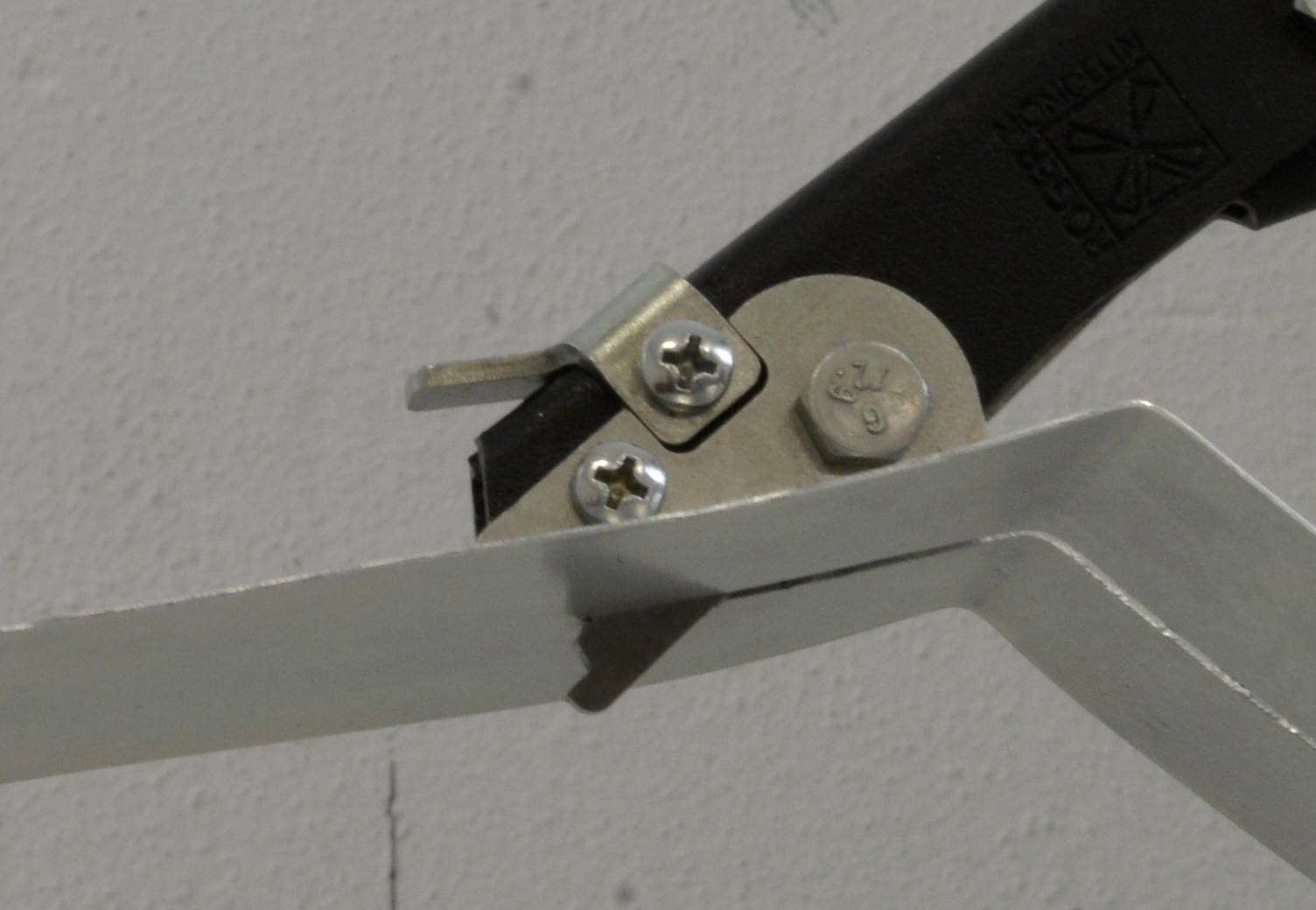 Nahaufnahme einer Metallhalterung und Schrauben, die einen schwarzen Arm an einem an der Wand montierten weißen Rahmen befestigen.