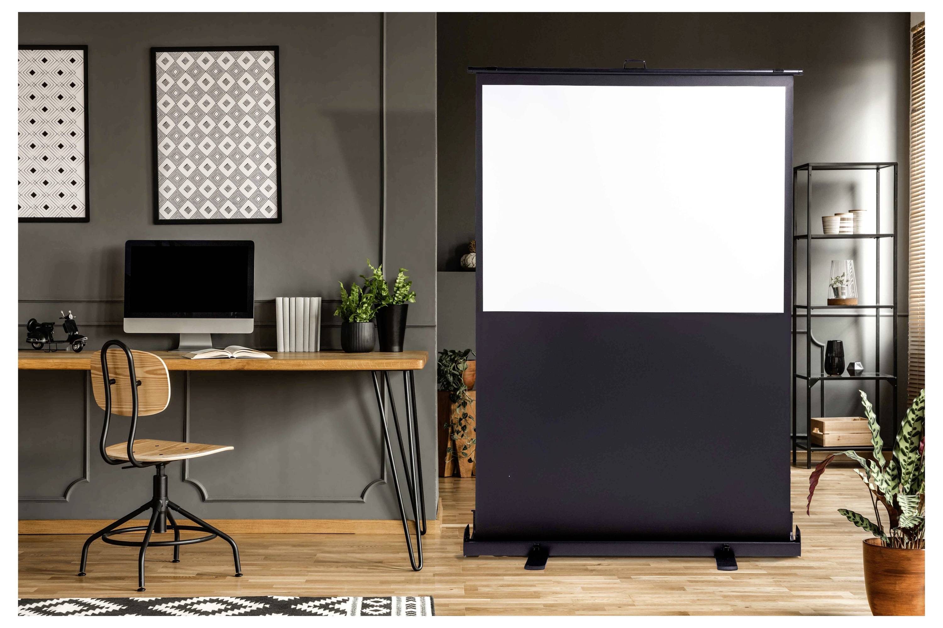 Homeoffice mit einer leeren ausfahrbaren Projektionsleinwand neben einem Schreibtisch, Stuhl, Computer und Dekoration, was auf ein Präsentations- oder Arbeitsbereich-Setup hindeutet.
