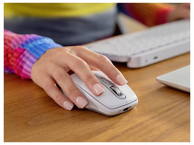 Nahaufnahme einer Hand einer Person, die eine weiße Computermaus auf einem Holzschreibtisch neben einer Tastatur und einem Laptop benutzt.
