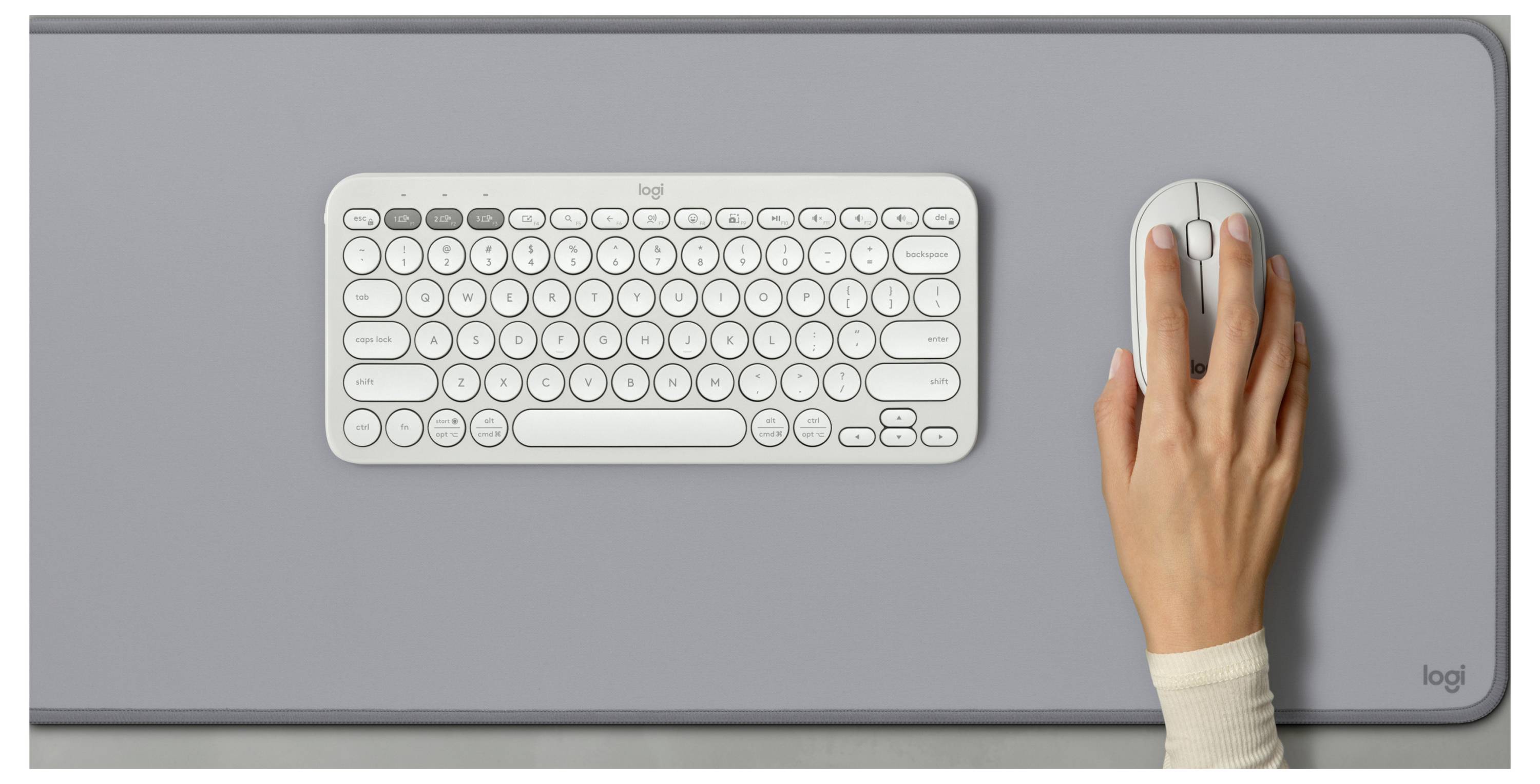 Draufsicht auf eine weiße kompakte Tastatur und eine rechte Hand, die eine Maus auf einer grauen Schreibunterlage verwendet.