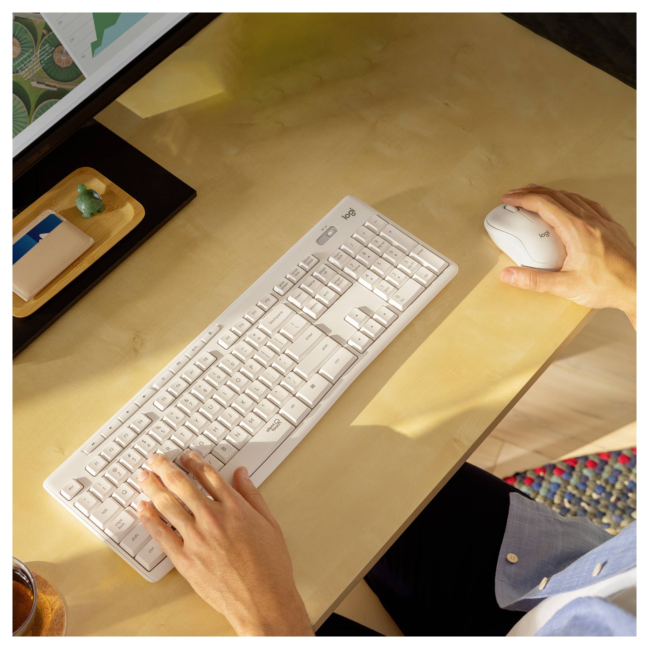 Draufsicht auf eine Person, die auf einer weißen Tastatur tippt und eine Maus an einem Schreibtisch im warmen Sonnenlicht benutzt.