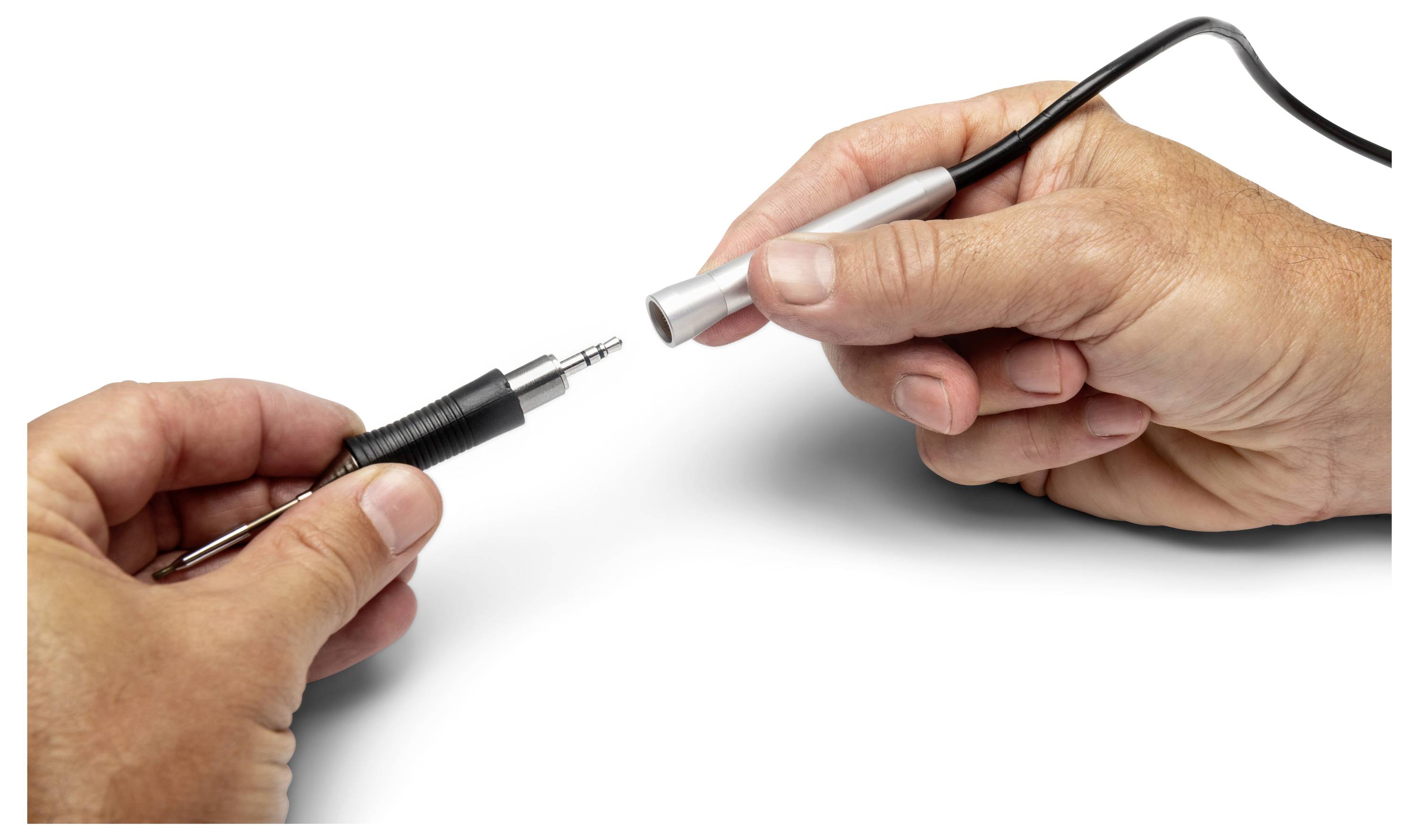 Hände verbinden einen schwarzen Audiostecker mit einem silbernen Adapter auf weißem Hintergrund.