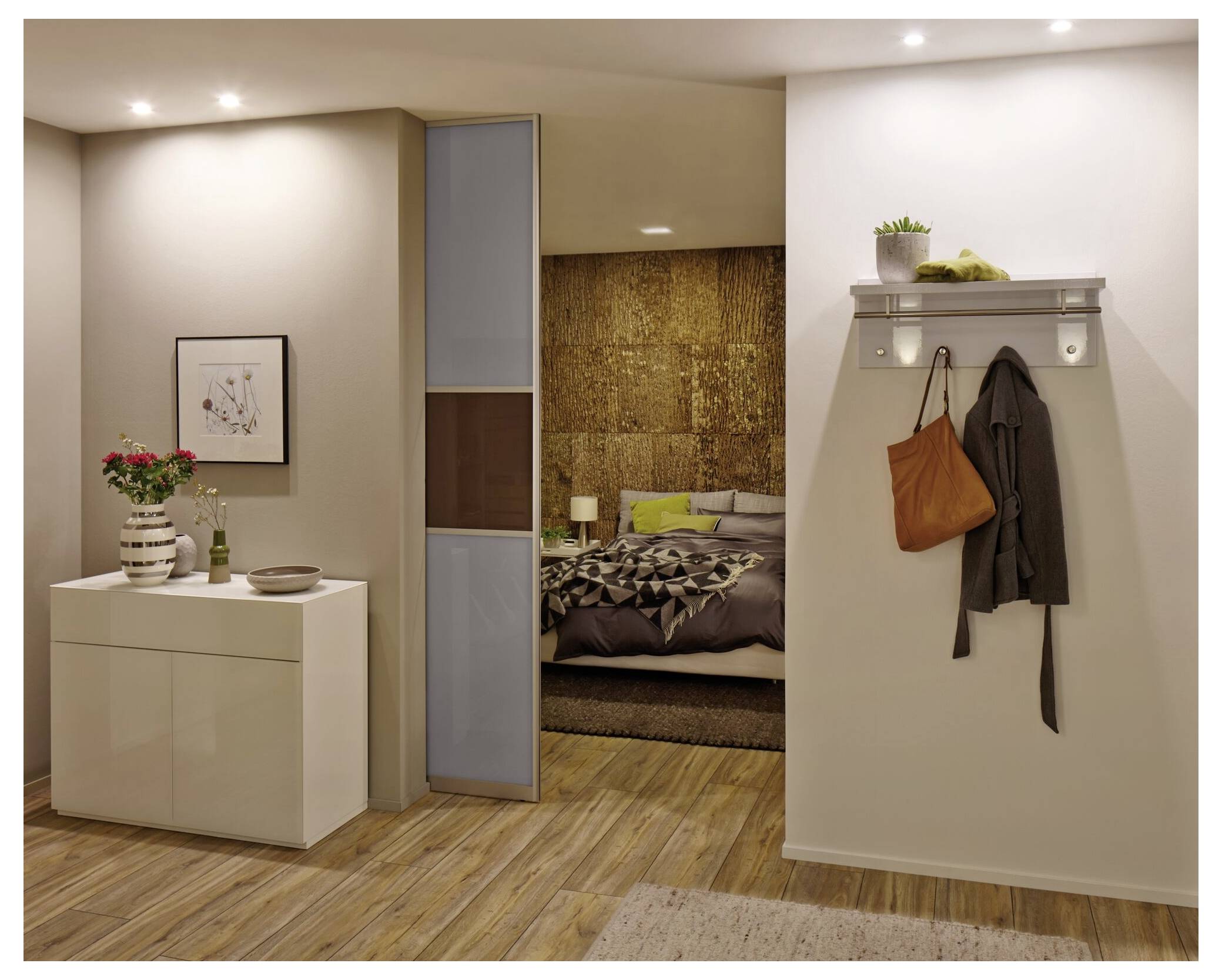 Moderner Apartment-Eingangsbereich, der sich zu einem Schlafzimmer öffnet, mit weißem Schrank und Wandregal neben der Tür und Mänteln, die an der rechten Wand hängen.