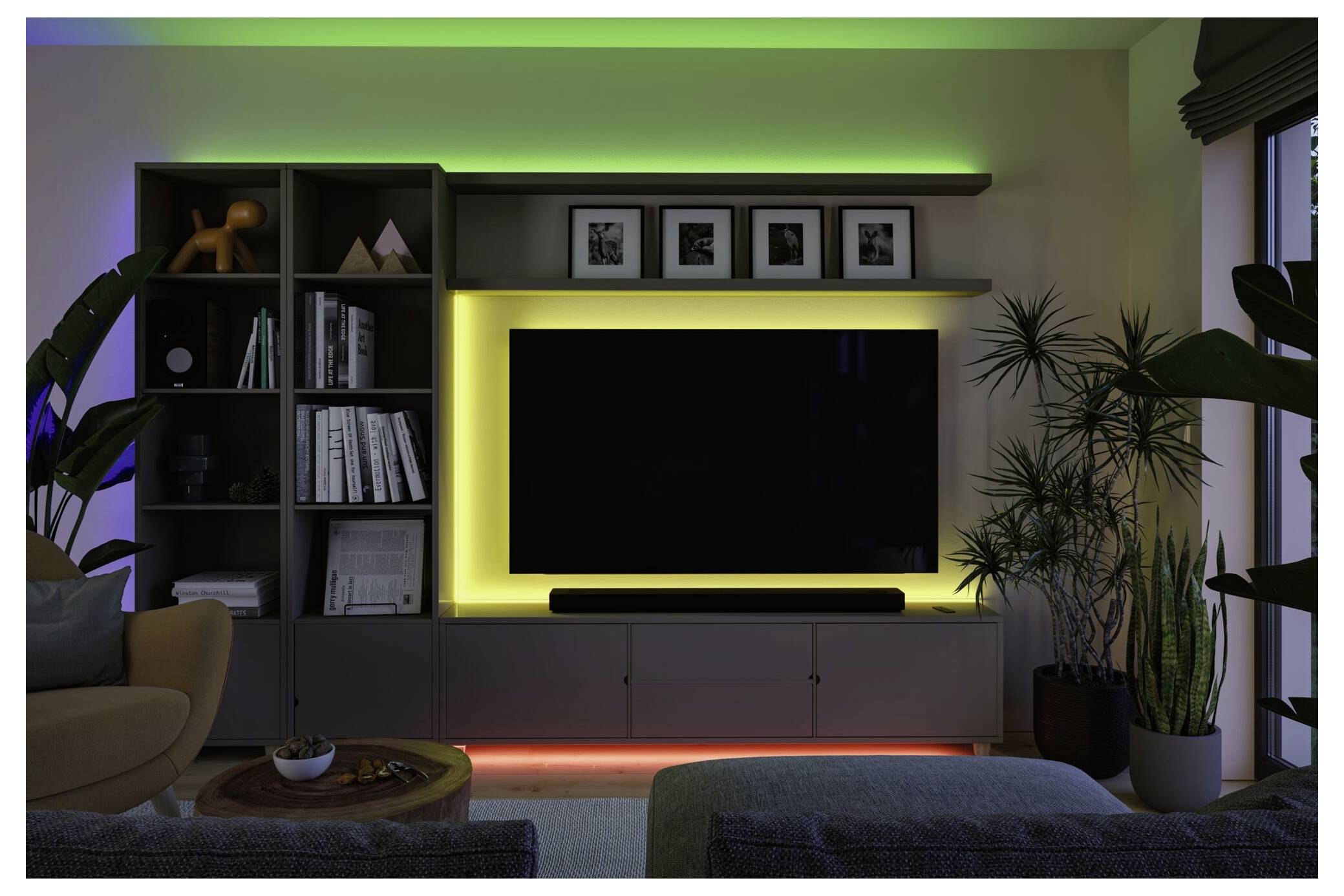 Modernes Wohnzimmer mit einem wandmontierten Fernseher, der in einer Regaleinheit zentriert ist, leuchtender gelber und grüner LED-Akzentbeleuchtung, Pflanzen und gerahmter Kunst darüber.