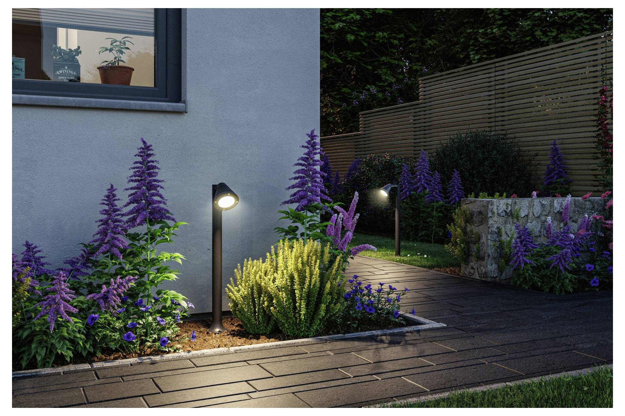 Moderner gestalteter Garten in der Dämmerung mit leuchtenden Weglichtern, violetten Blumen und einem hölzernen Gehweg neben einem Haus.