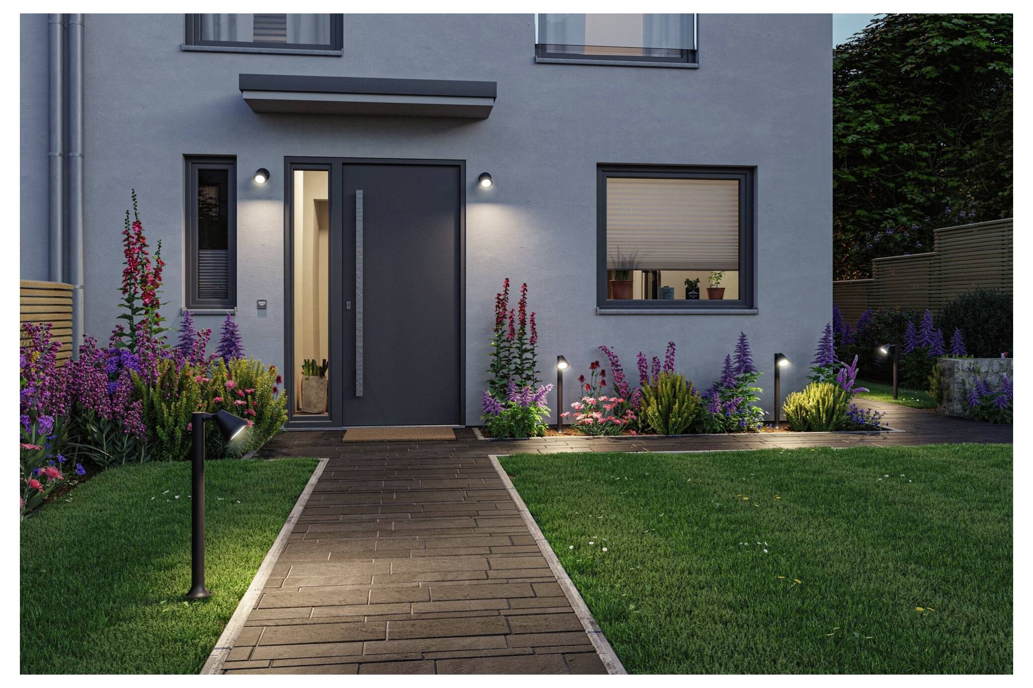 Modernes Hausäußeres in der Dämmerung mit beleuchteter Haustür, Steingehweg und angelegtem Garten mit Blumen und Rasen.