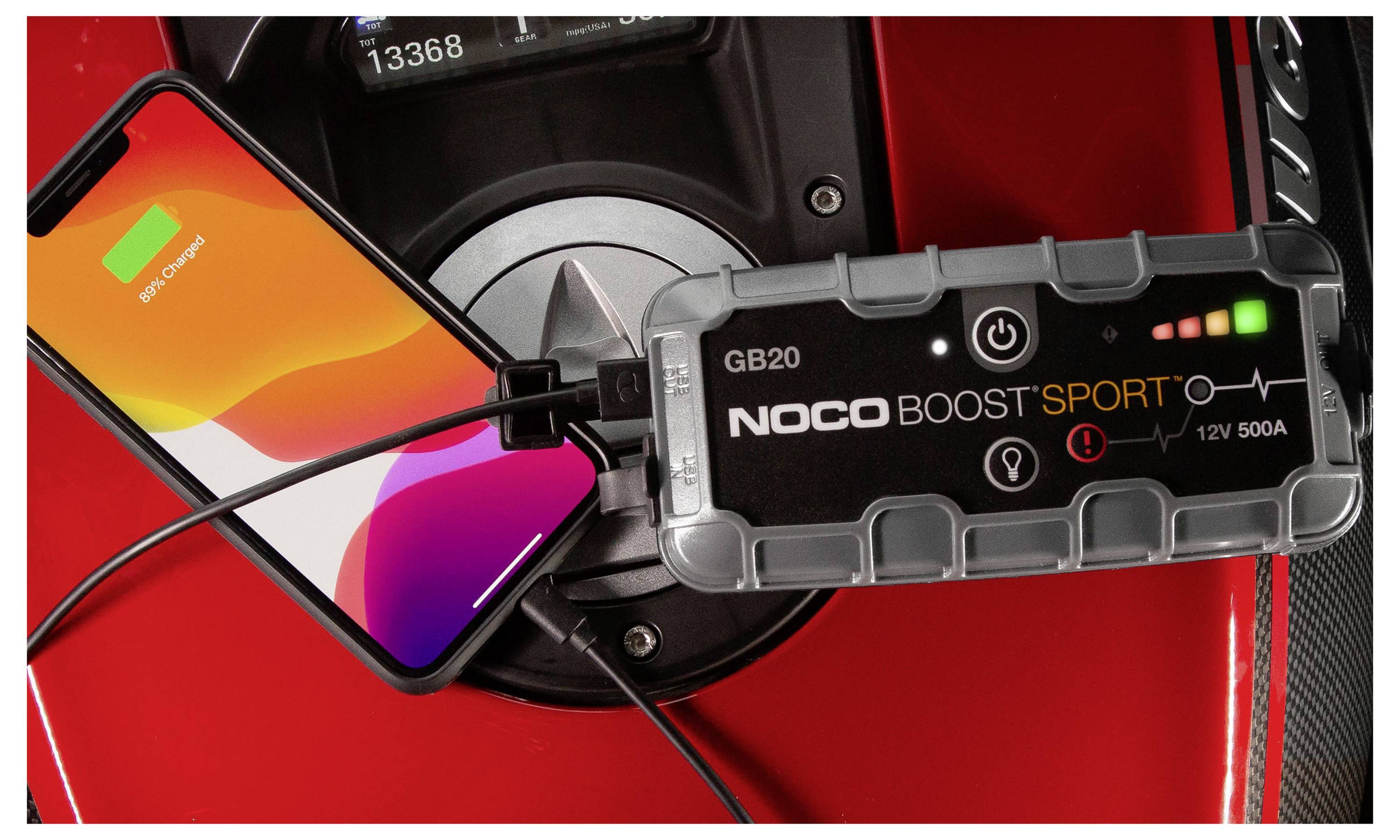 Smartphone verbunden mit einem NOCO Boost Sport GB20 Starthilfegerät in einem roten Autoinnenraum, mit Strom- und Ladekabeln.