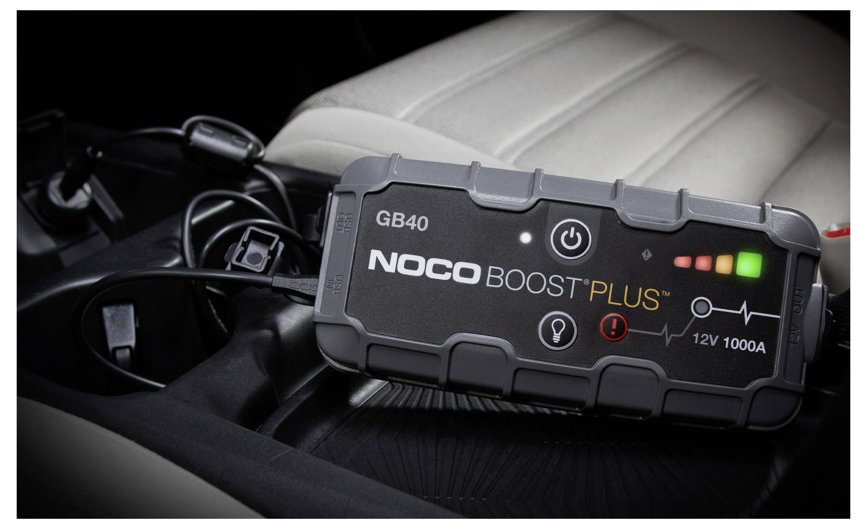 NOCO Boost Plus GB40 tragbarer Starthilfegerät mit beleuchteten Stromanzeigen ruht auf einem Autositz, mit angeschlossenen Kabeln in der Nähe.