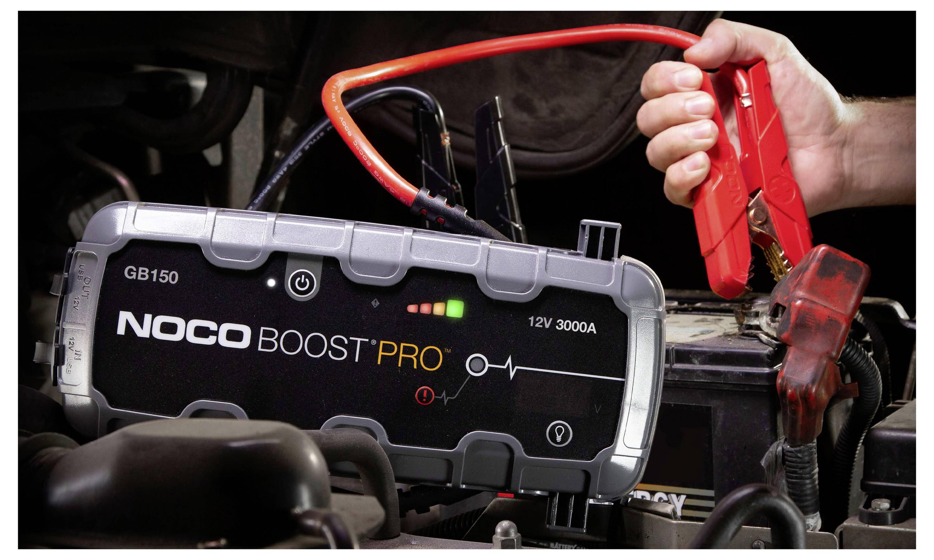 Tragbarer NOCO Boost Pro Starthilfegerät mit roten Klemmen an eine Autobatterie angeschlossen, wird zum Starten des Fahrzeugs verwendet