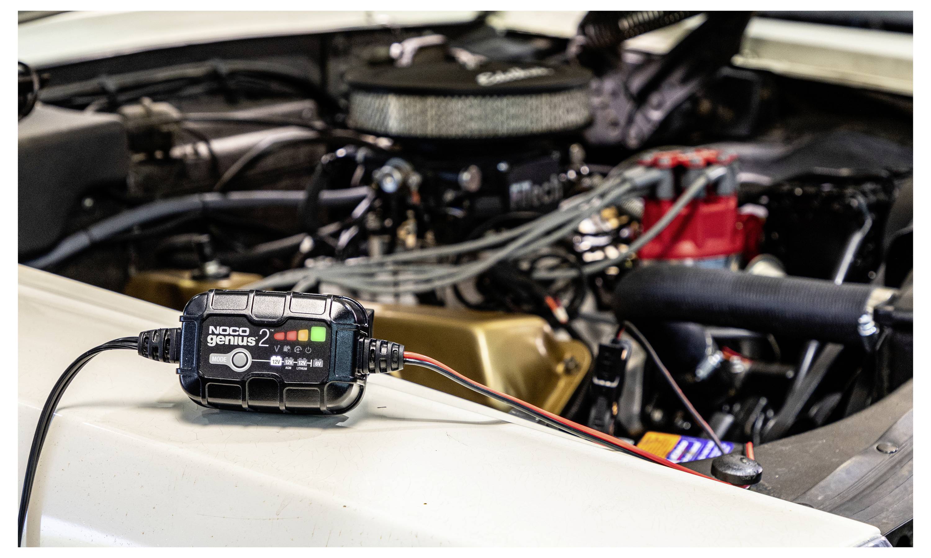 Autobatterie-Ladegerät, das mit dem Motorraum eines Autos verbunden ist, mit Klemmen und Kabeln, die in der Nähe der Batterie und des Lufteinlasses angebracht sind.