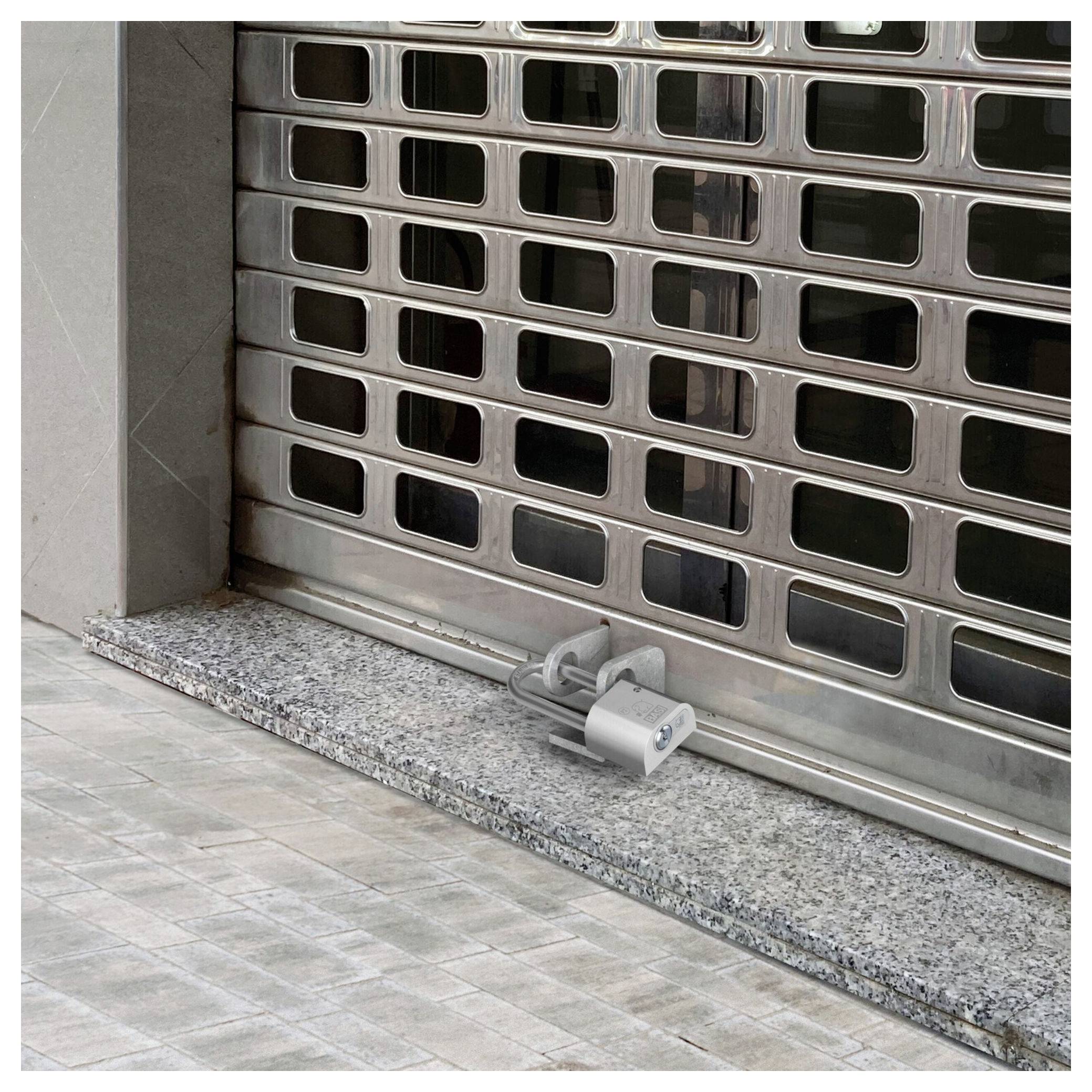 Geschlossenes Metallsicherheitsrolltor mit einem Vorhängeschloss am unteren Ende verriegelt, das einen Geschäftseneingang blockiert.