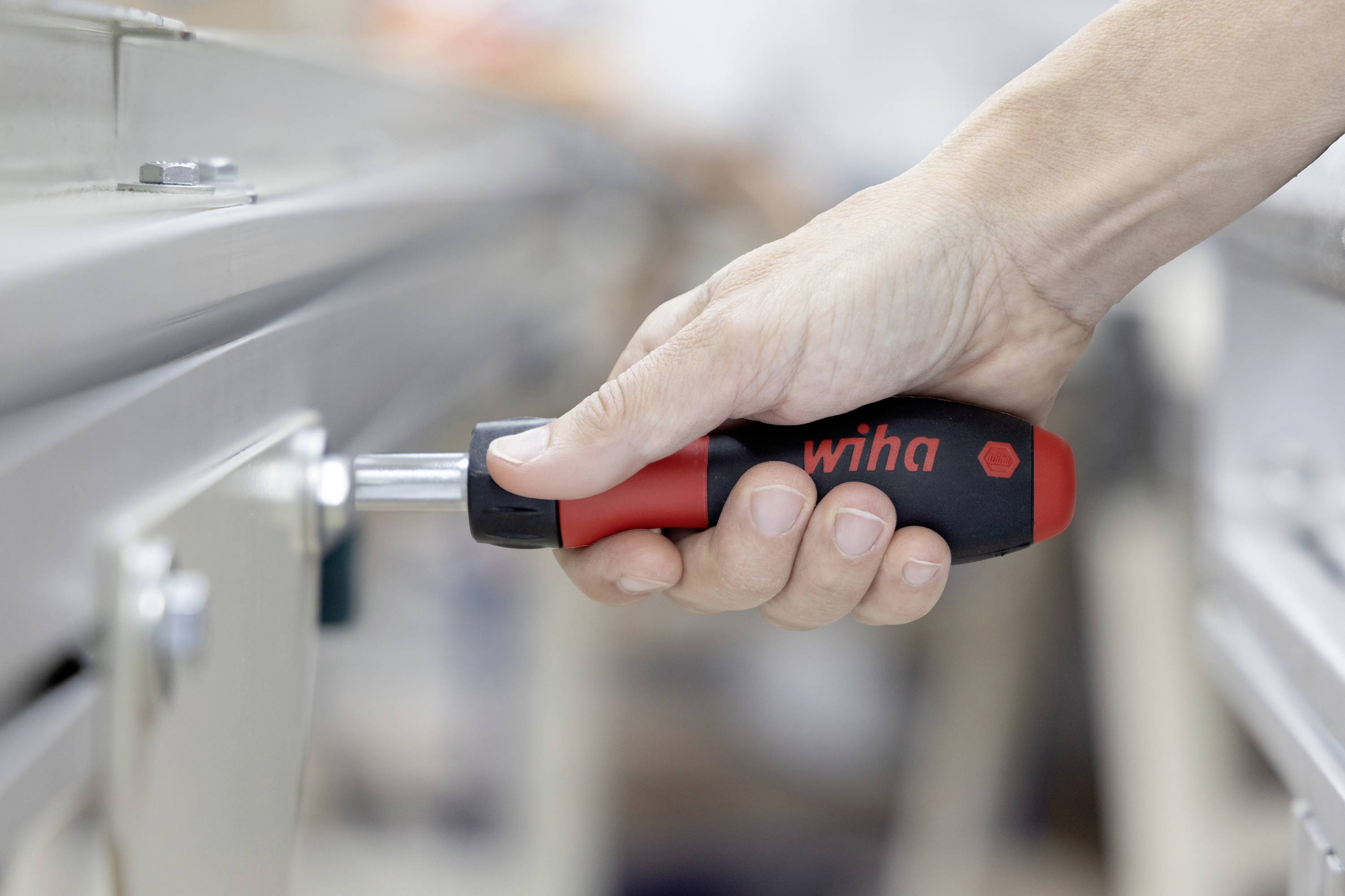 Nahaufnahme einer Hand, die einen Wiha-Schraubendreher verwendet, um ein Metallmaschinenpaneel oder eine Befestigung anzupassen.