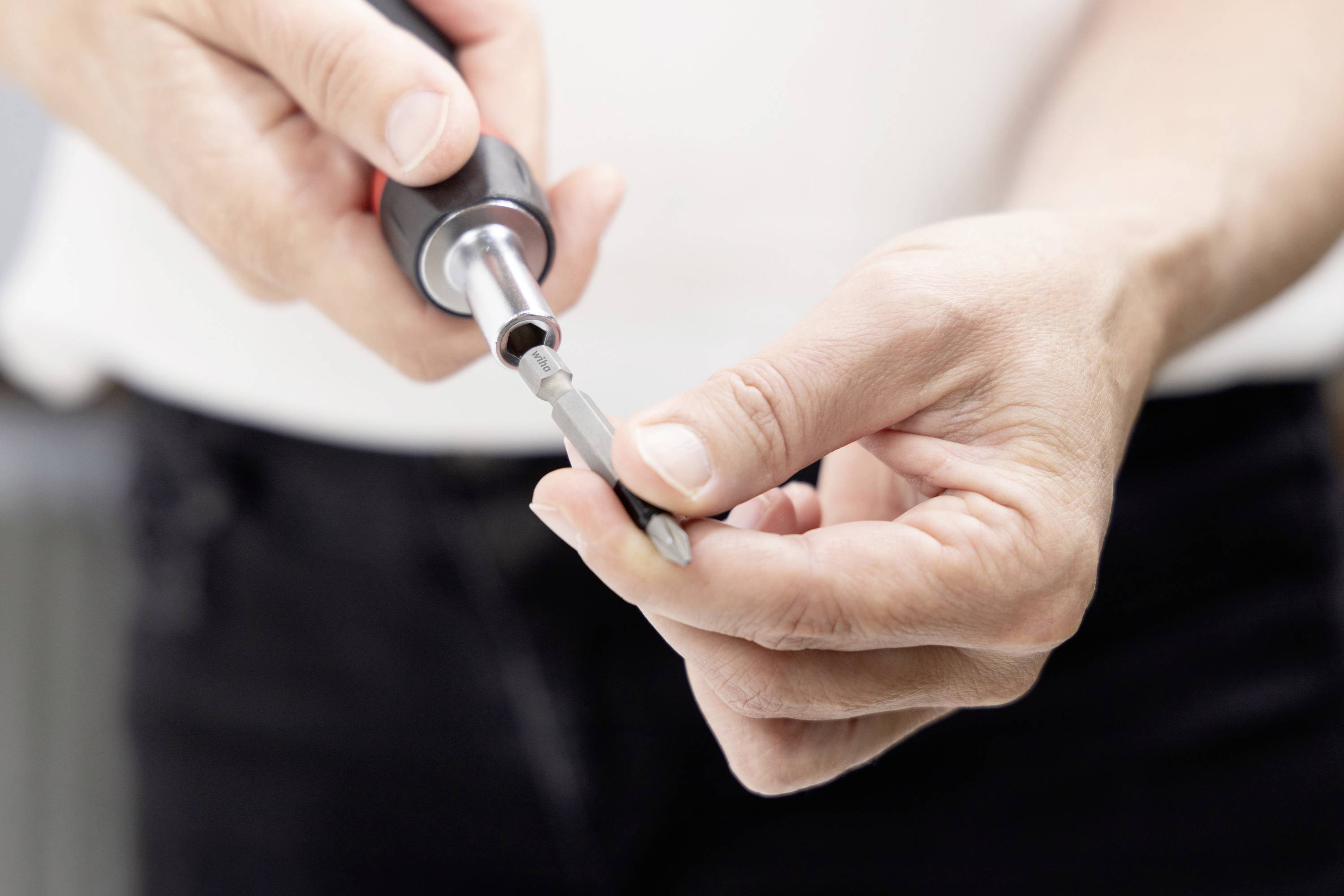 Nahaufnahme von Händen, die einen Schraubendreher verwenden, um ein kleines Gerät oder eine Komponente anzupassen oder zu reparieren.