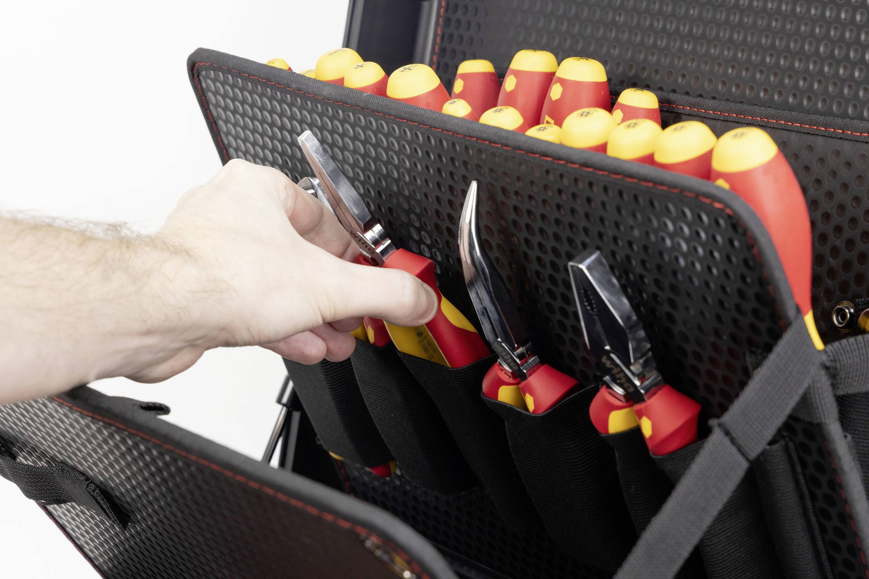 Hand, die rot-gelbe isolierte Zange in eine schwarze Werkzeugrolle mit mehreren ähnlichen, darin gelagerten Werkzeugen legt.