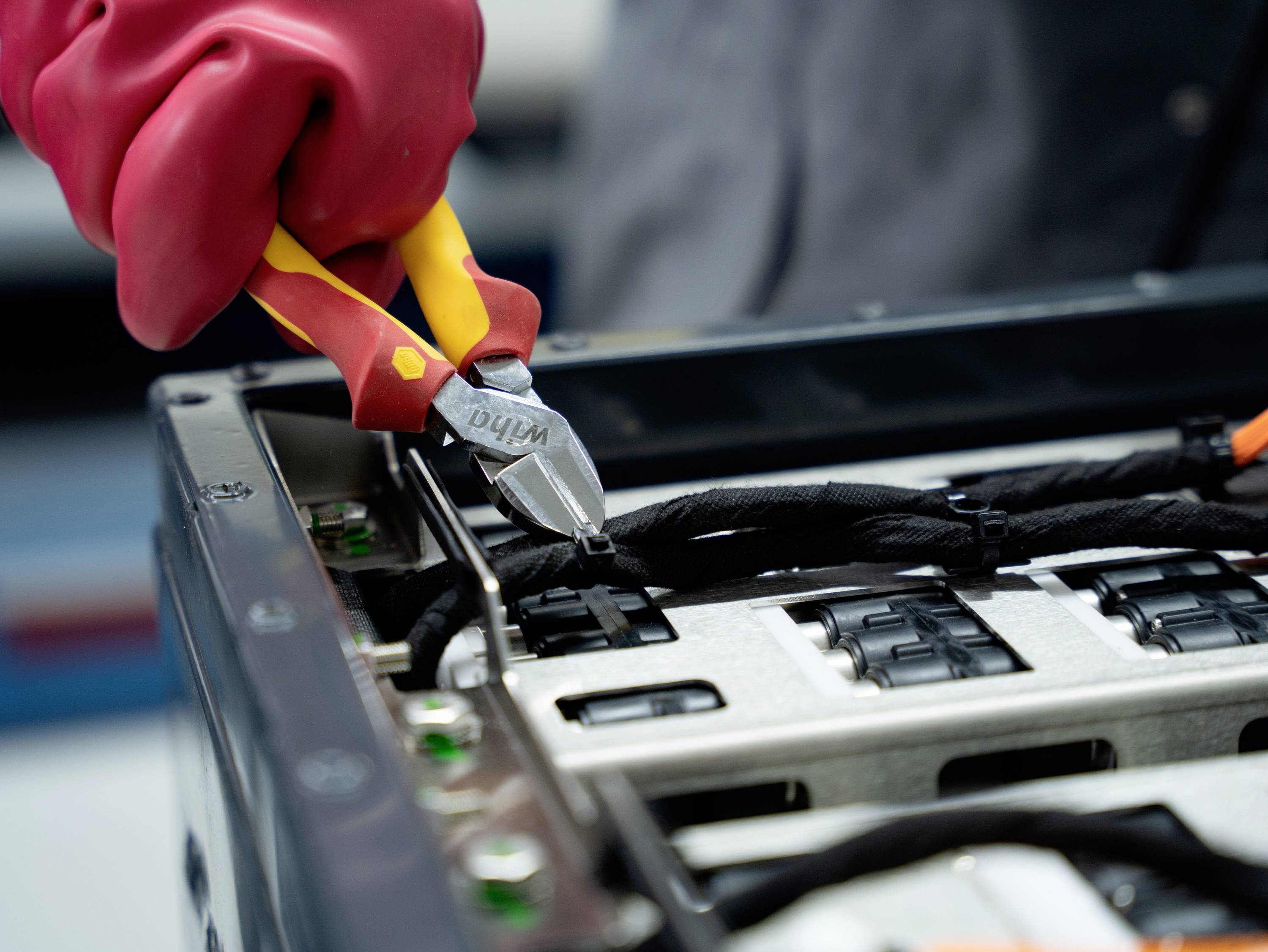 Eine behandschuhte Hand verwendet einen Seitenschneider, um Kabel in einem offenen elektronischen Gerät oder Server-Gehäuse zu durchtrennen.