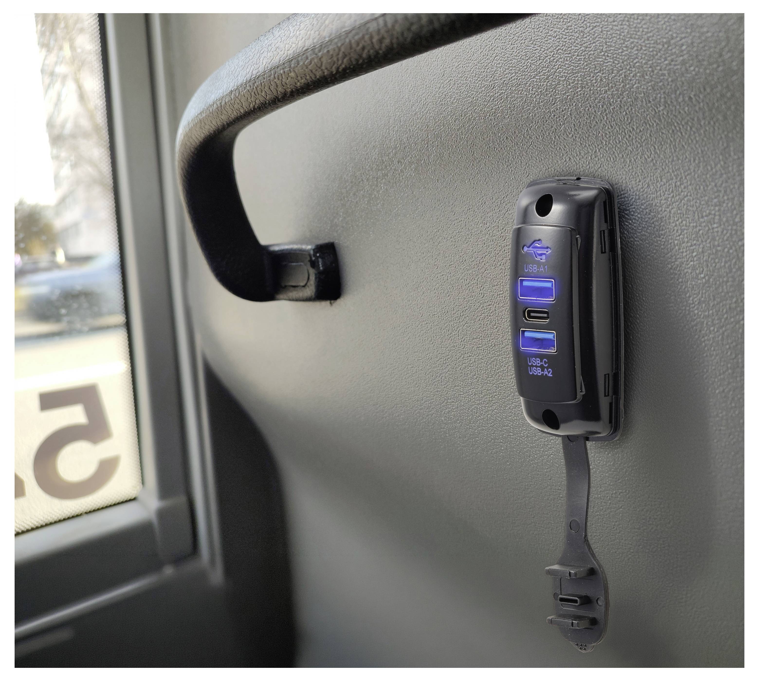 Ein Busfahrzeugsitz mit einem montierten USB-Stromadapter und Ladekabel neben einem Fenster.