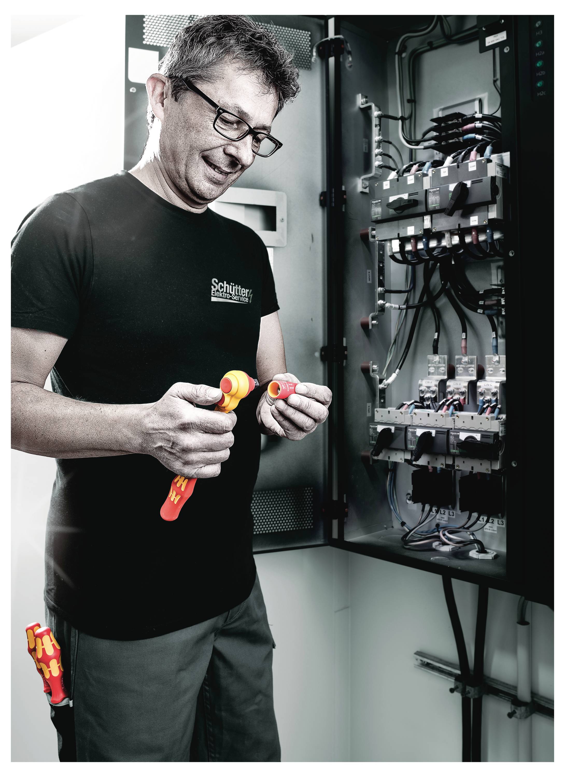 Techniker in einem Server- oder Elektrikschrank inspiziert und bedient Verdrahtungswerkzeuge in einem offenen Bedienfeld.