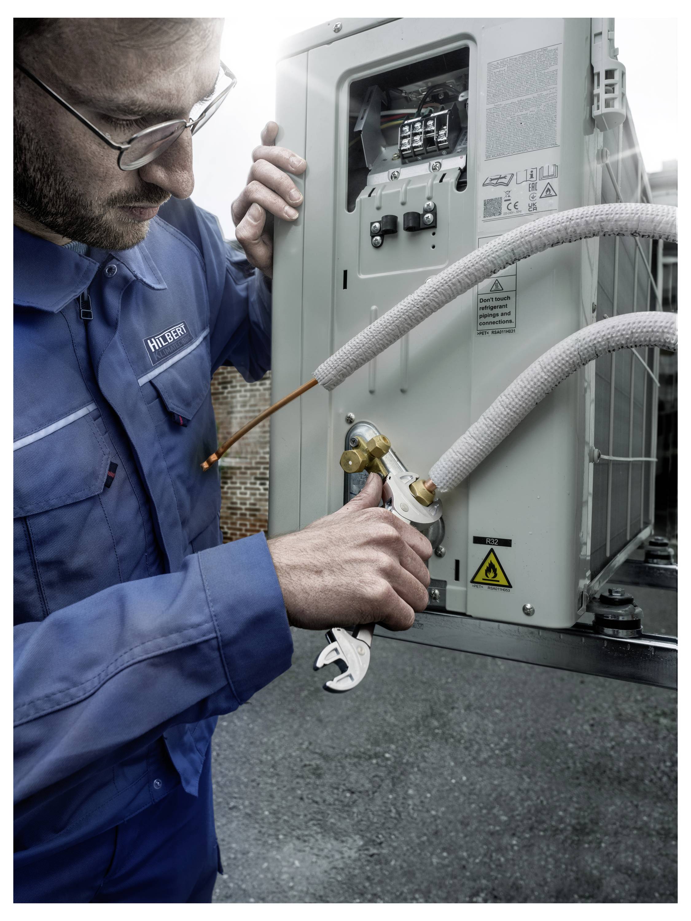 Techniker in blauen Overalls inspiziert und justiert die Verdrahtung an einem Außen-Elektrosteugerät mit Schlauchverbindungen.