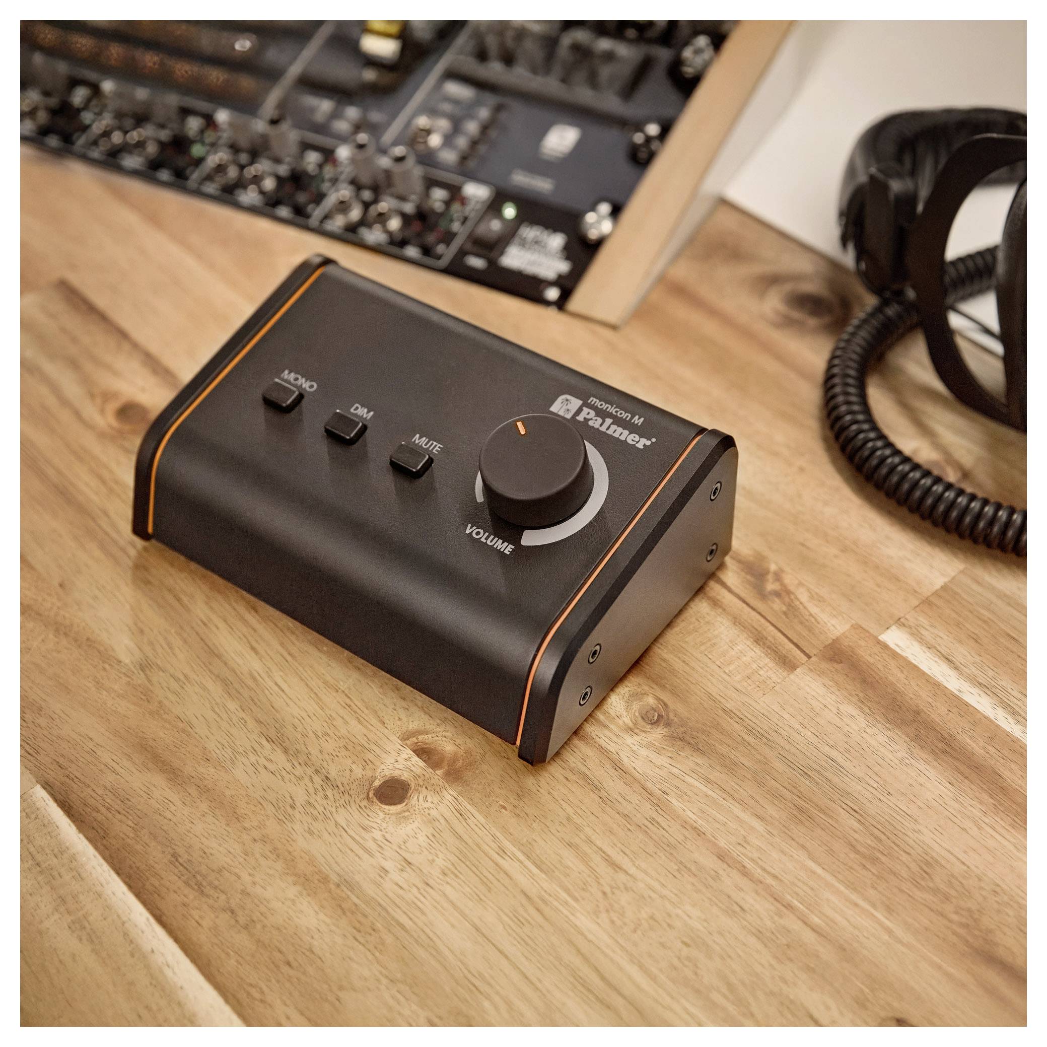 Schwarze Desktop-Audiokontrollbox auf einem Holztisch, mit Lautstärkeregler und Mono-, Dim- und Stumm-Tasten.