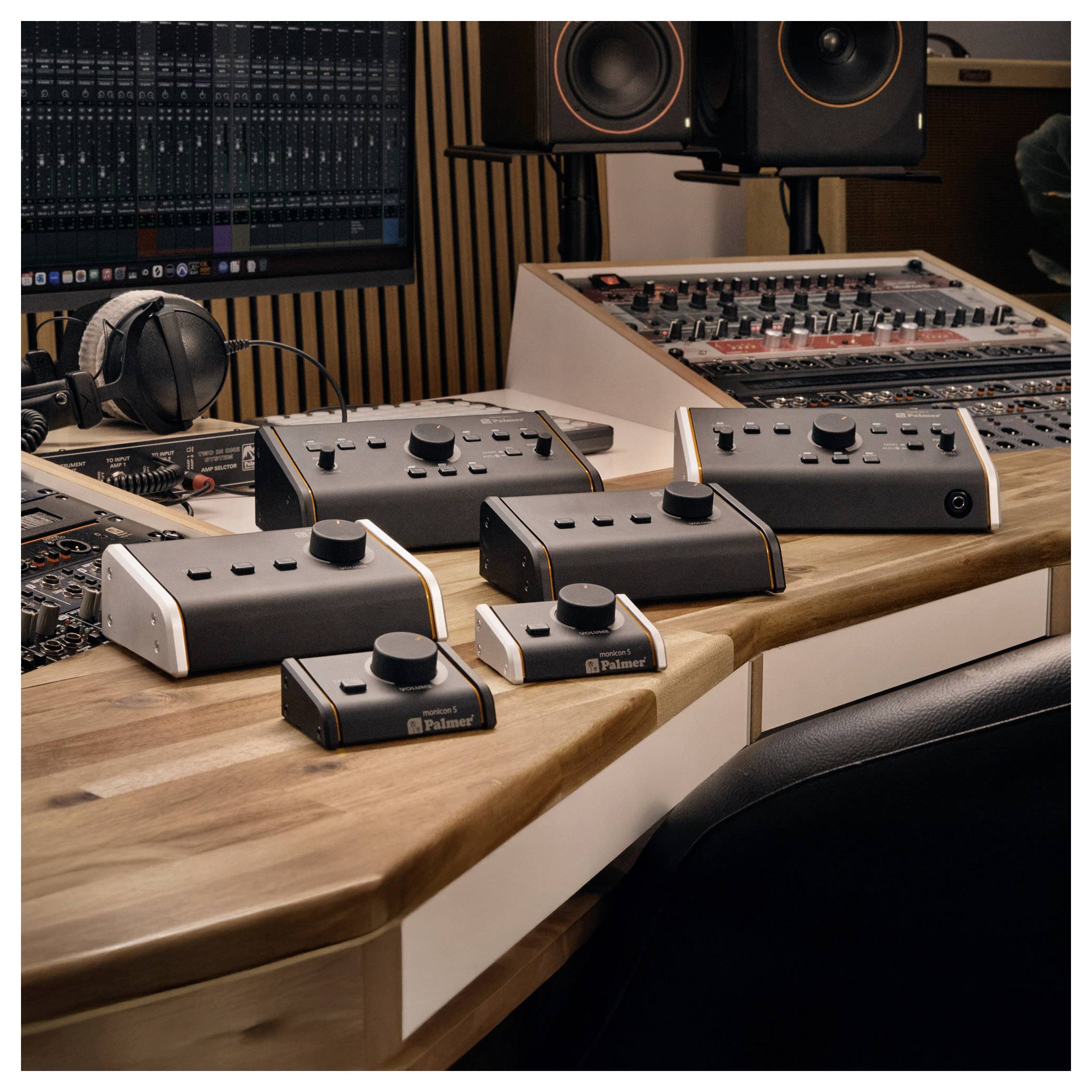 Audioproduktionspult mit mehreren schwarz-weißen Kontrollelementen und Reglern auf einer Holztischplatte, umgeben von Studiomonitoren und Mischpulten.