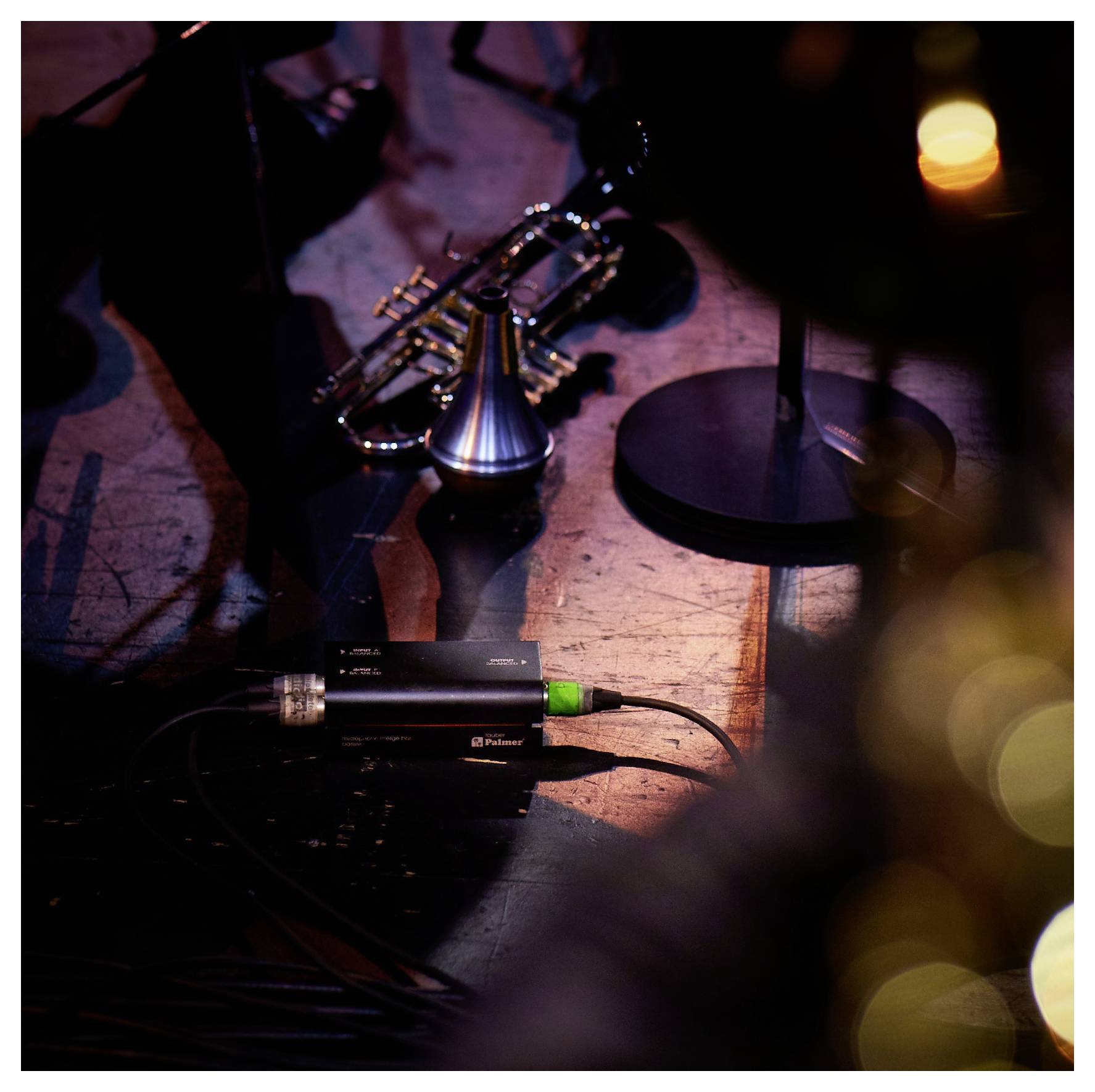 Eine Trompete und ein Mikrofon auf einer schwach beleuchteten Bühne, mit einem warmen, kerzenlichtähnlichen Licht im Hintergrund, das ein Setup für eine Live-Musikaufführung andeutet.