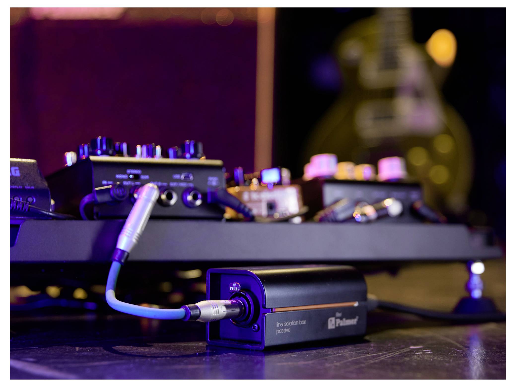 Nahaufnahme eines Gitarren-Pedalboards mit mehreren Effektpedalen und einem angeschlossenen Instrumentenkabel auf einem Bühnen- oder Studioboden.