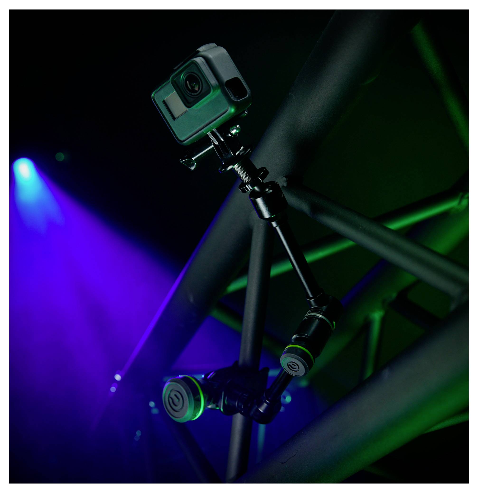Action-Kamera montiert auf einer verstellbaren Stange oder einem Gimbal, beleuchtet von blauen und grünen Bühnenscheinwerfern vor dunklem Hintergrund.