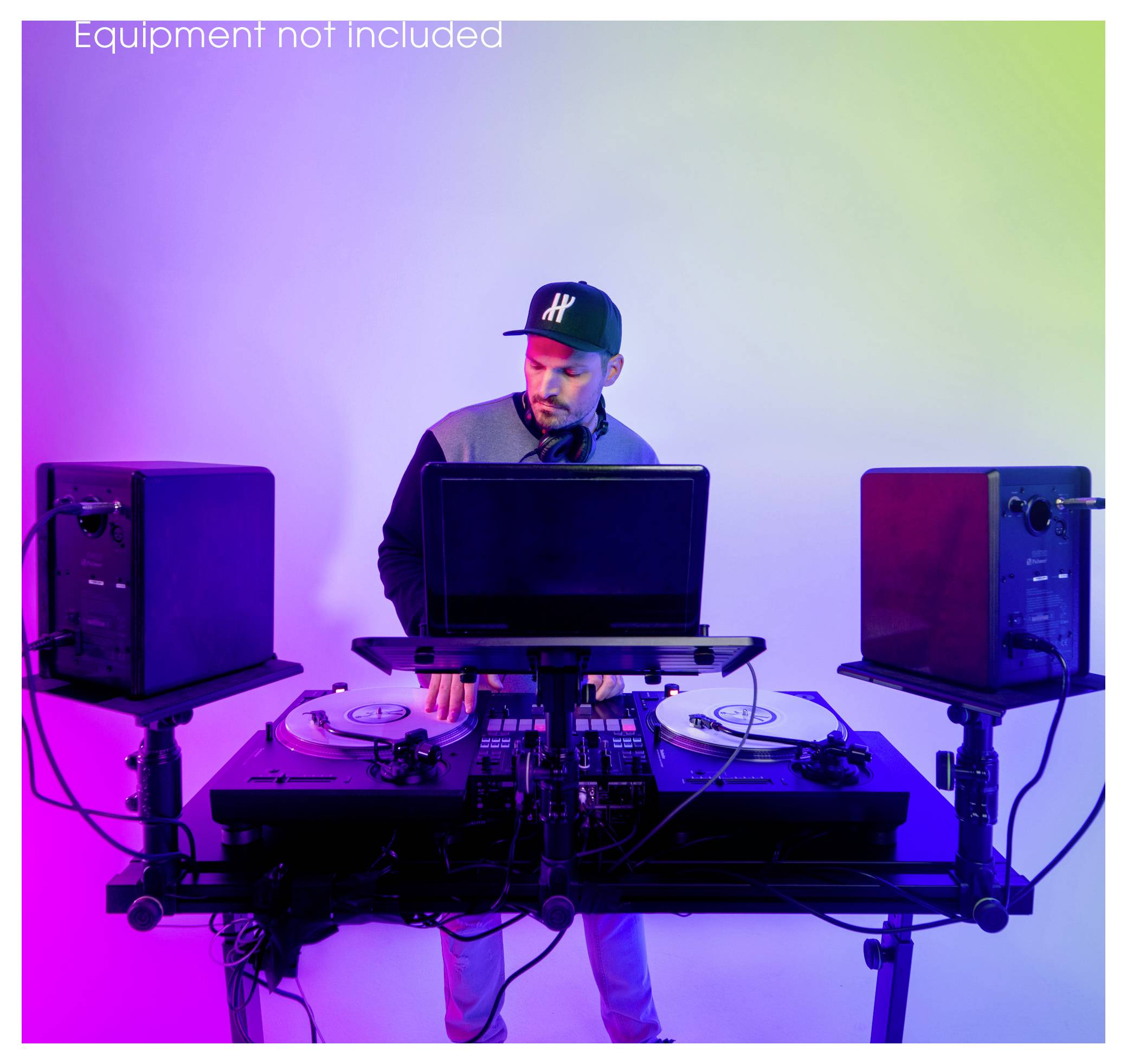 DJ, der auf doppelten Plattenspielern und einem Mischer hinter einem Laptop auftritt, flankiert von Lautsprechern, unter violett-blauem Licht.