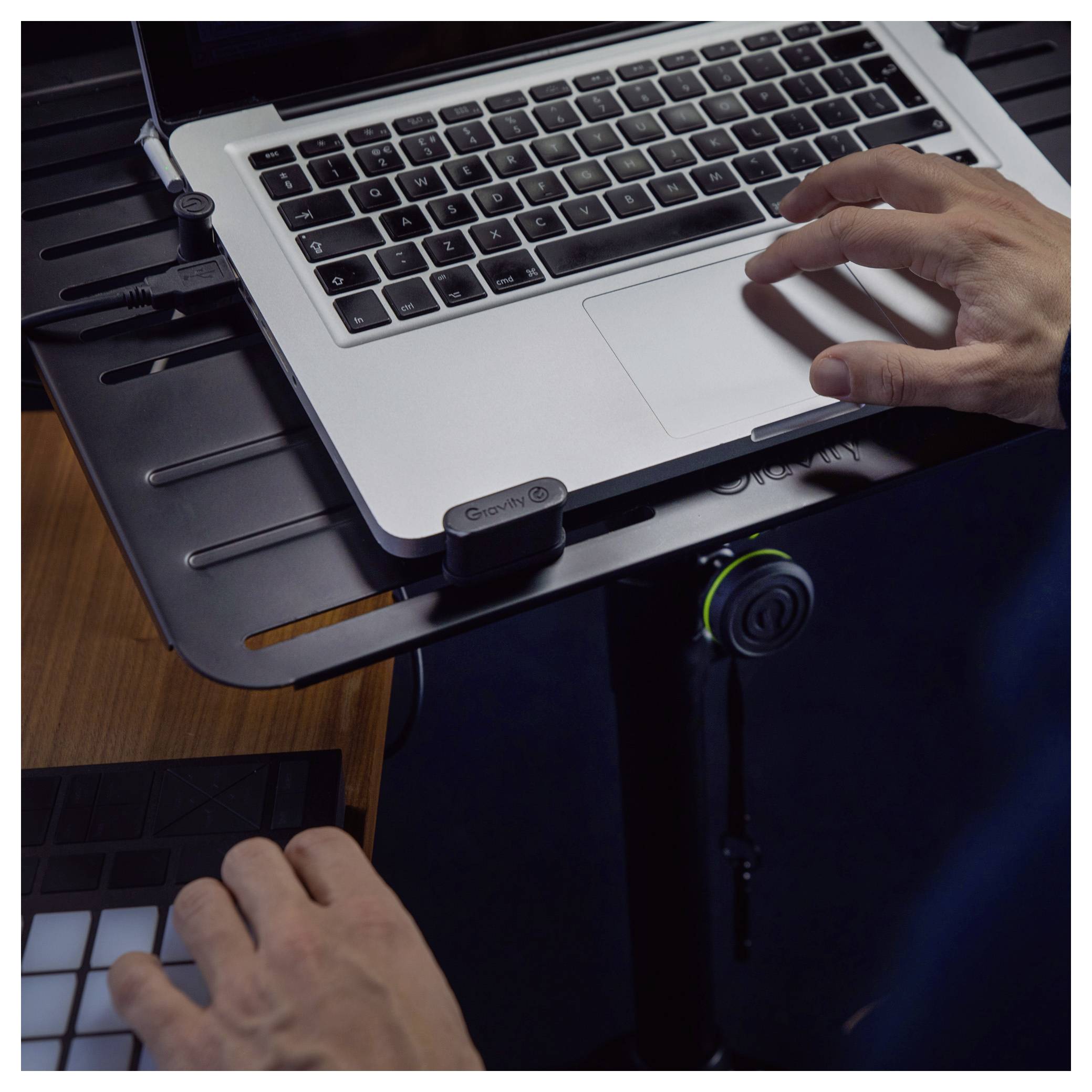 Hände, die einen Laptop auf einem Ständer und einen MIDI-Controller verwenden, was auf Musikproduktion oder Live-Mixing hindeutet.